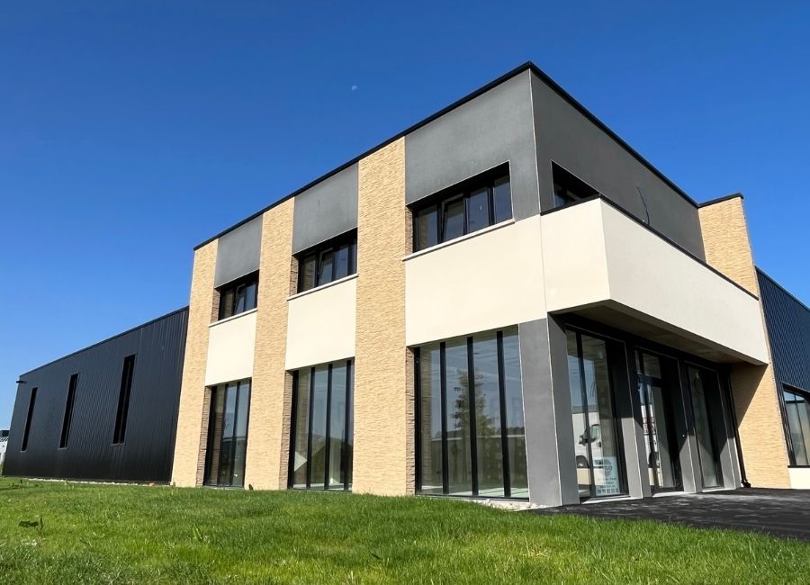 Vue d’angle d’un bâtiment de bureaux avec façade en enduit clair et bardage métallique.