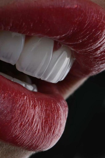 Nahaufnahme von glänzenden roten Lippen, die teilweise geöffnet sind und weiße Zähne vor einem dunklen Hintergrund zeigen.