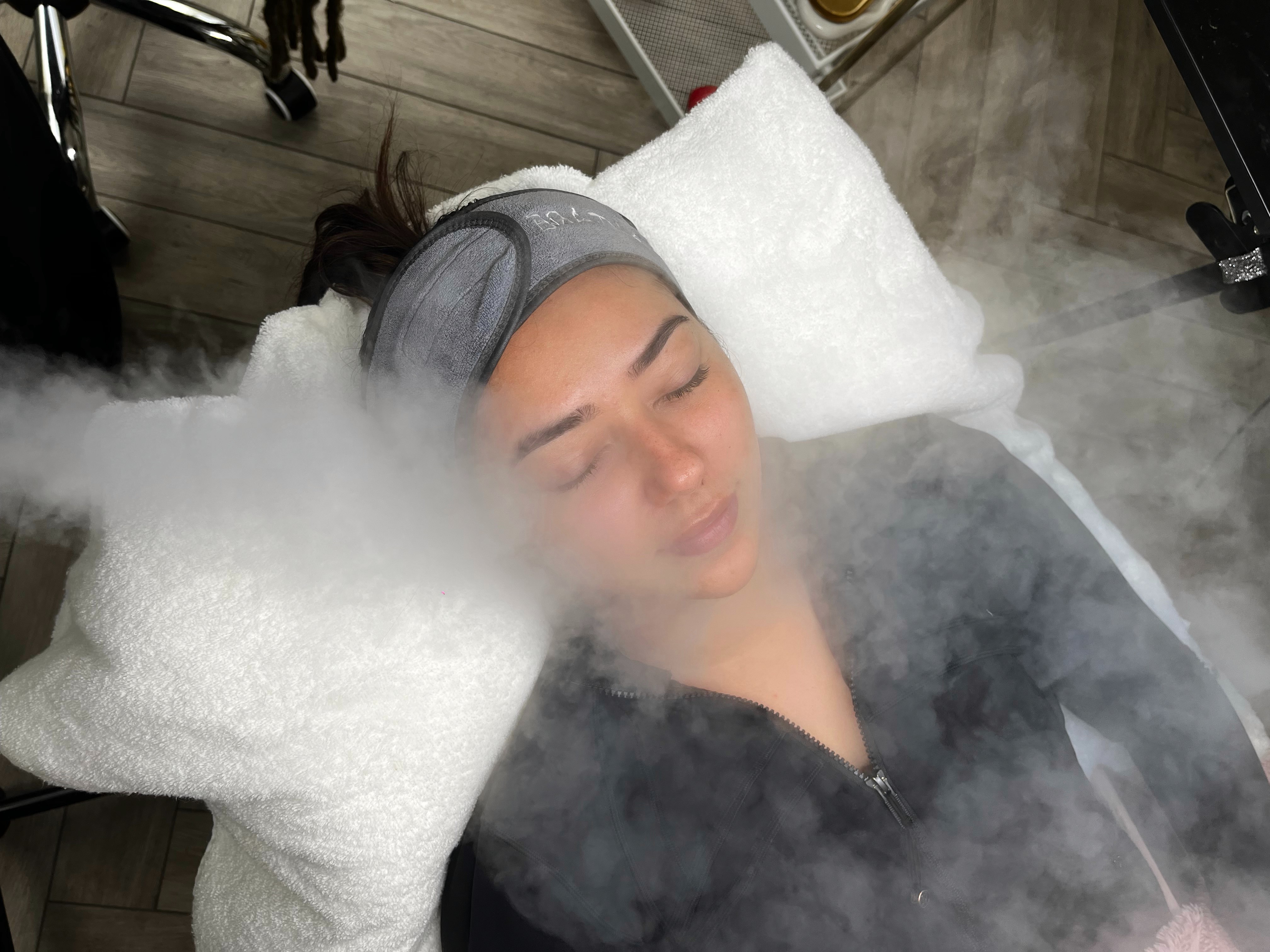 A person lies on a pillow, eyes closed, surrounded by mist or vapor, creating a serene atmosphere.