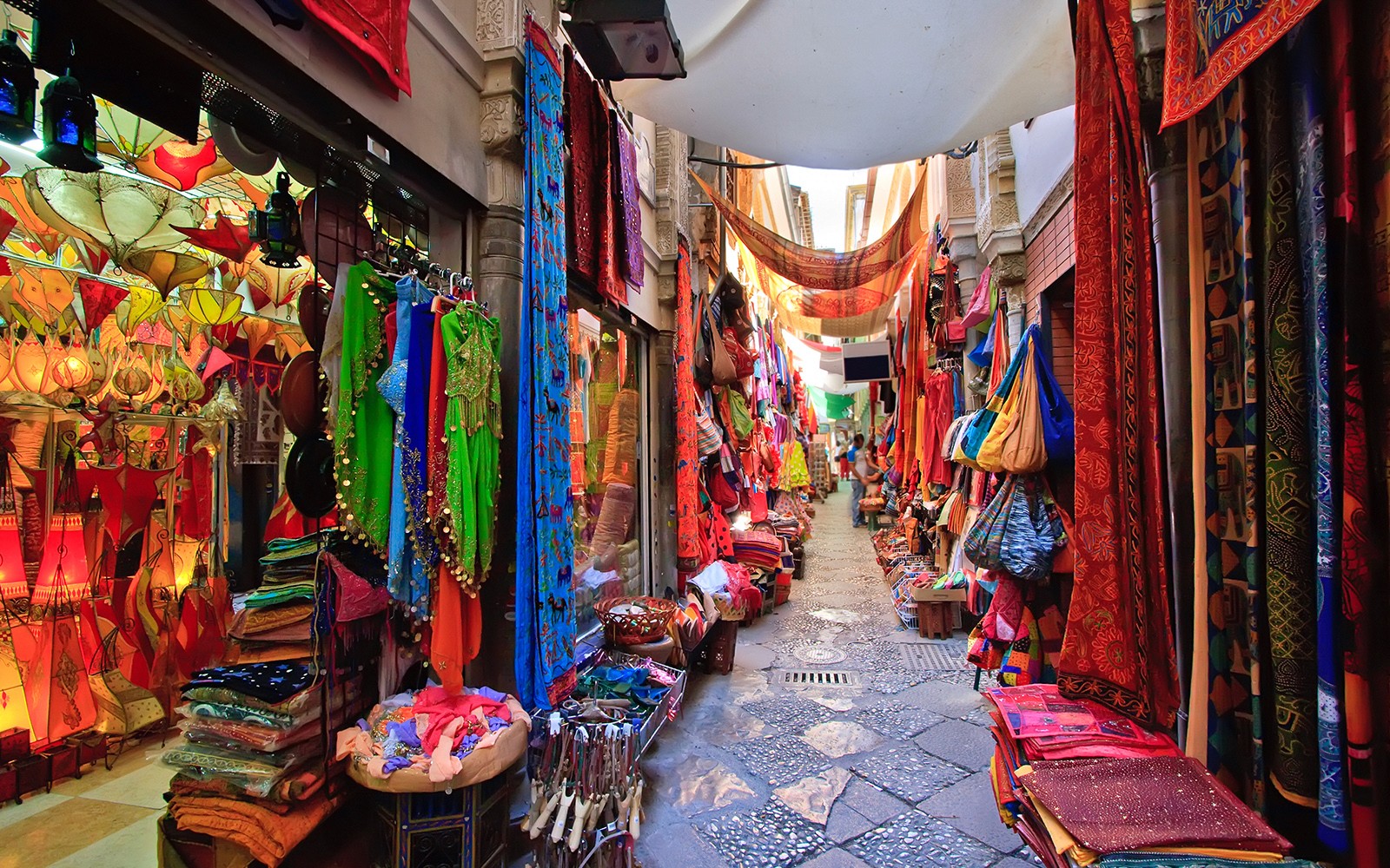 Colorful market street in Albaicin, Granada, with vibrant textiles and lanterns on display.