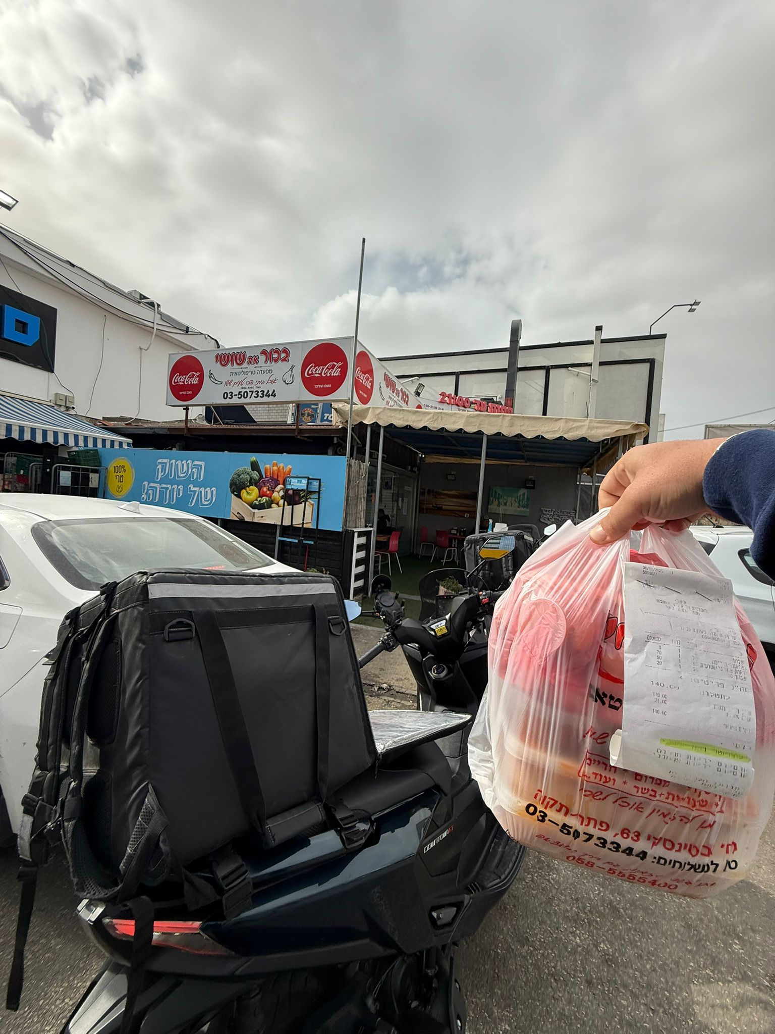 שקית משלוח עם קבלה מוחזקת ליד אופנוע חונה.