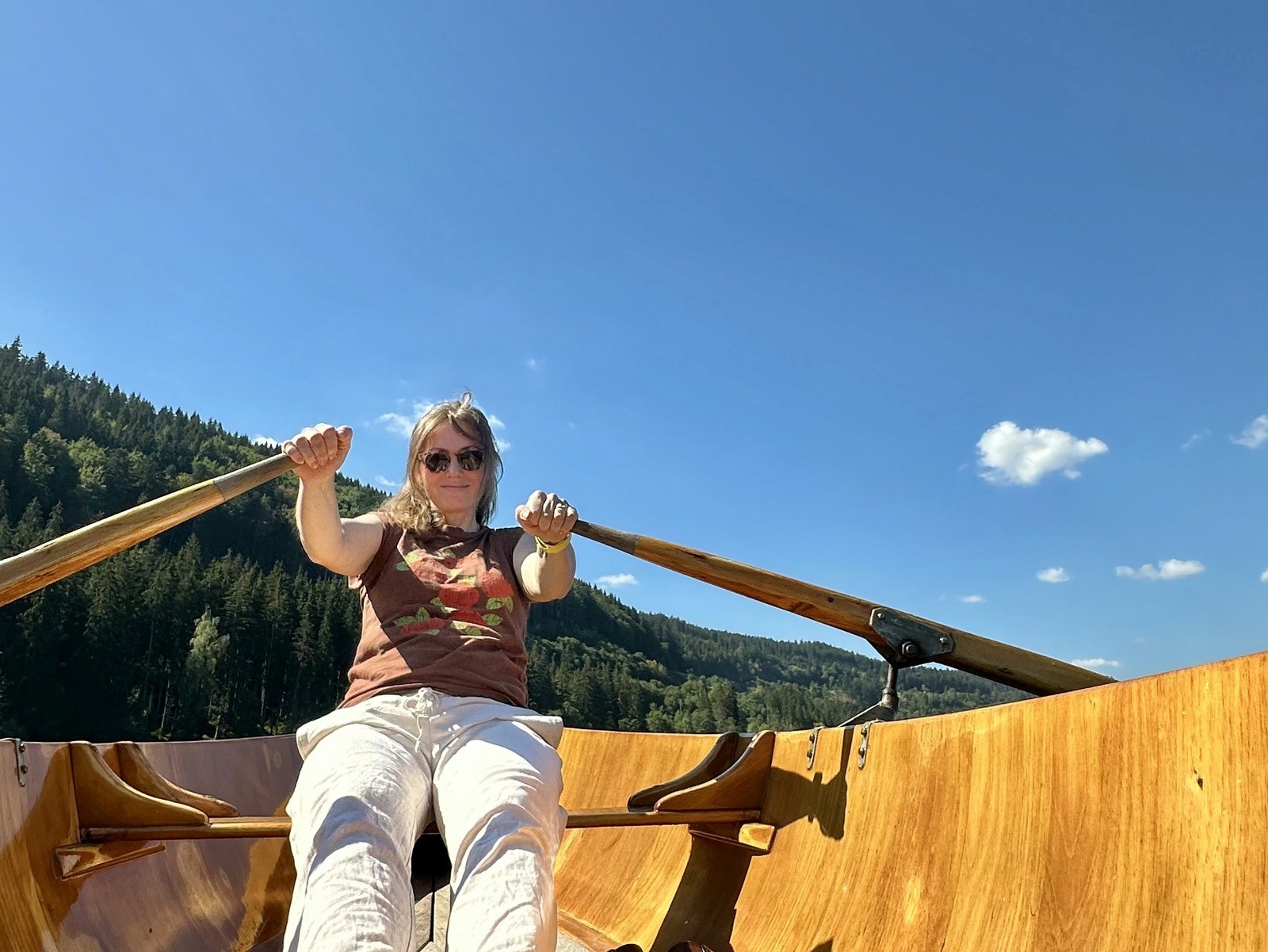 A woman rows a wooden boat across the calm waters of Titisee, surrounded by forested hills.