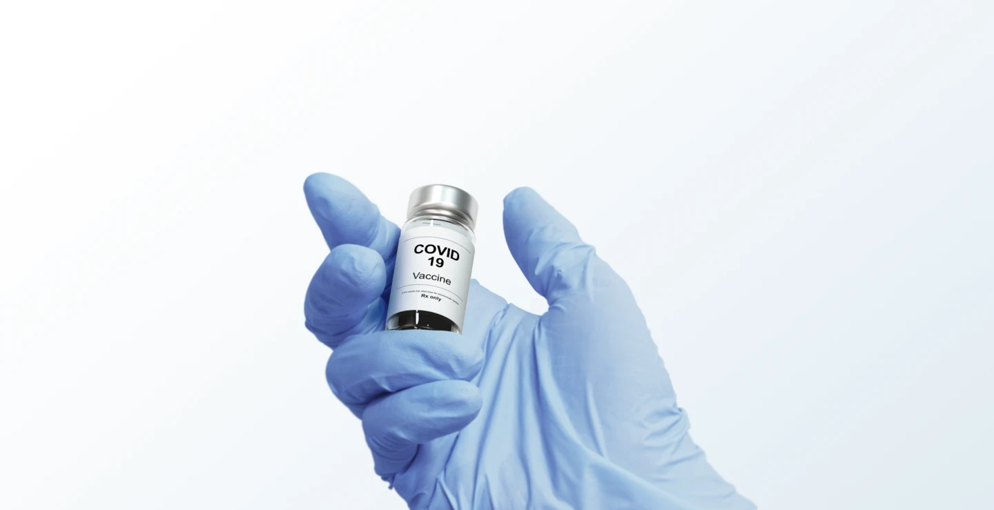 Image of a hand wearing a blue glove holding a COVID vaccine