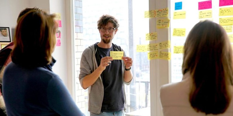 A workshop facilitator showcasing a post-it note to a group of workshop participants 