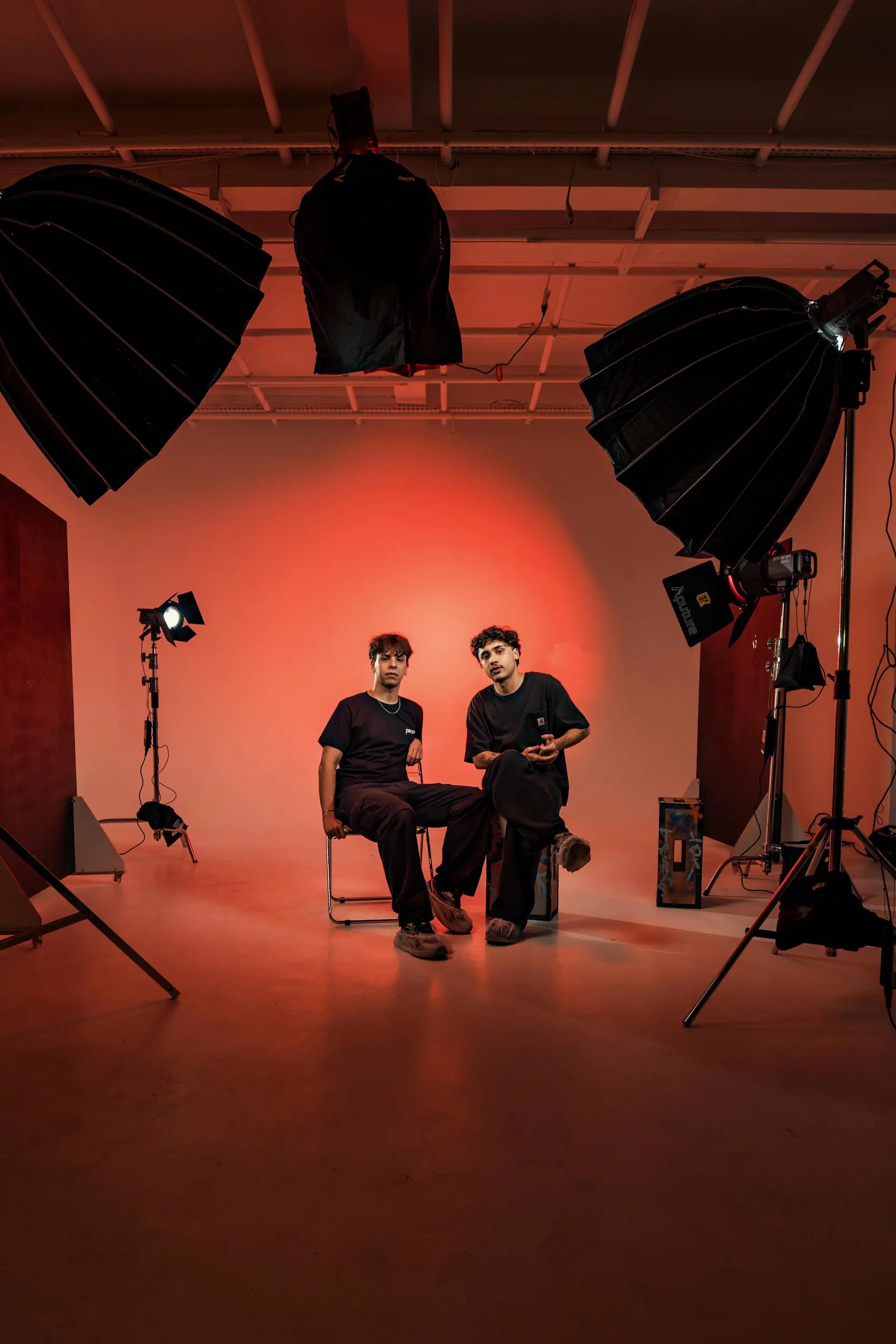 Two men sitting in a photography studio with large softbox lights and a vibrant red glow on the wall.