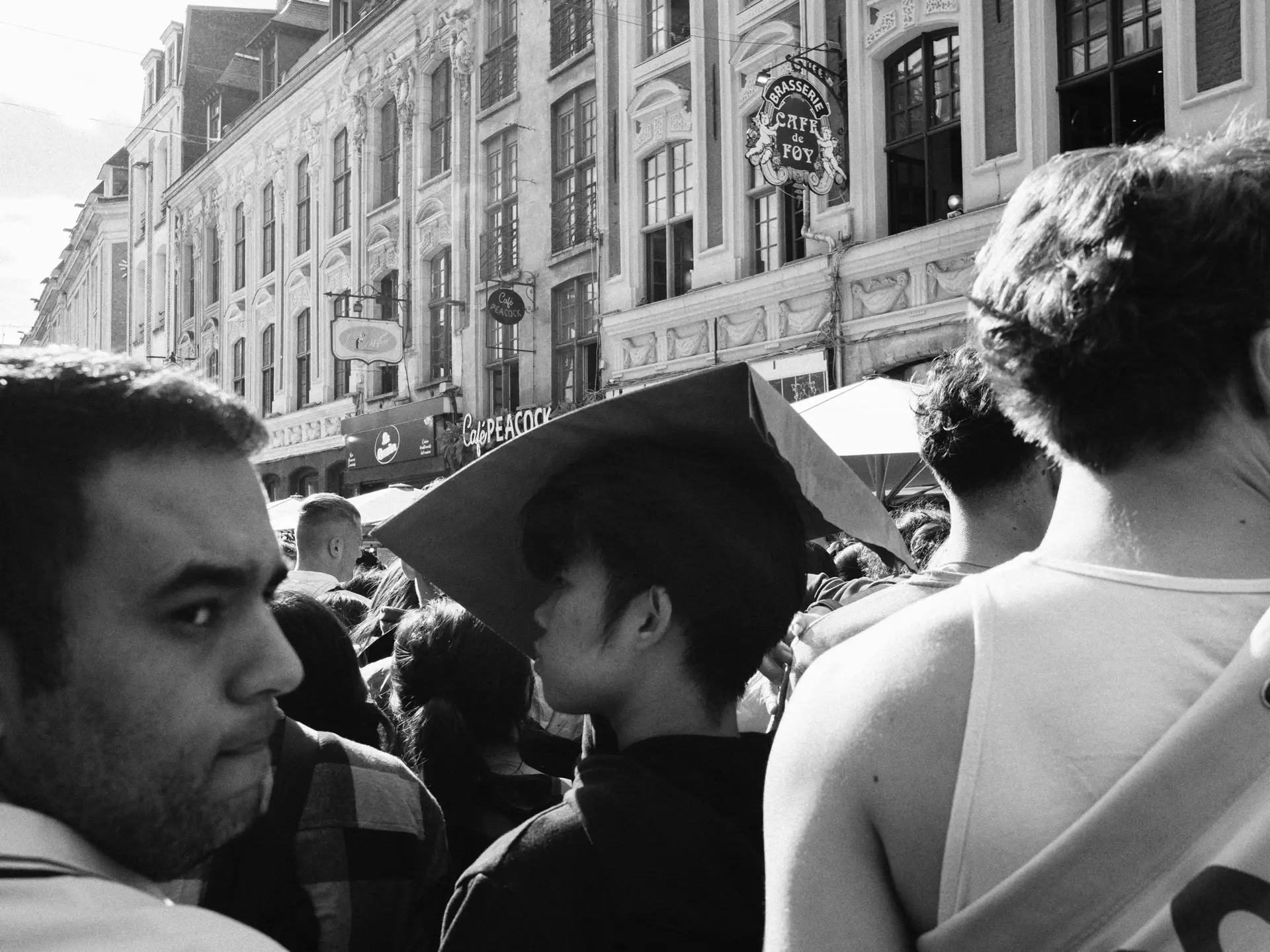 Dense crowd on a street lined with historic facades, in black and white