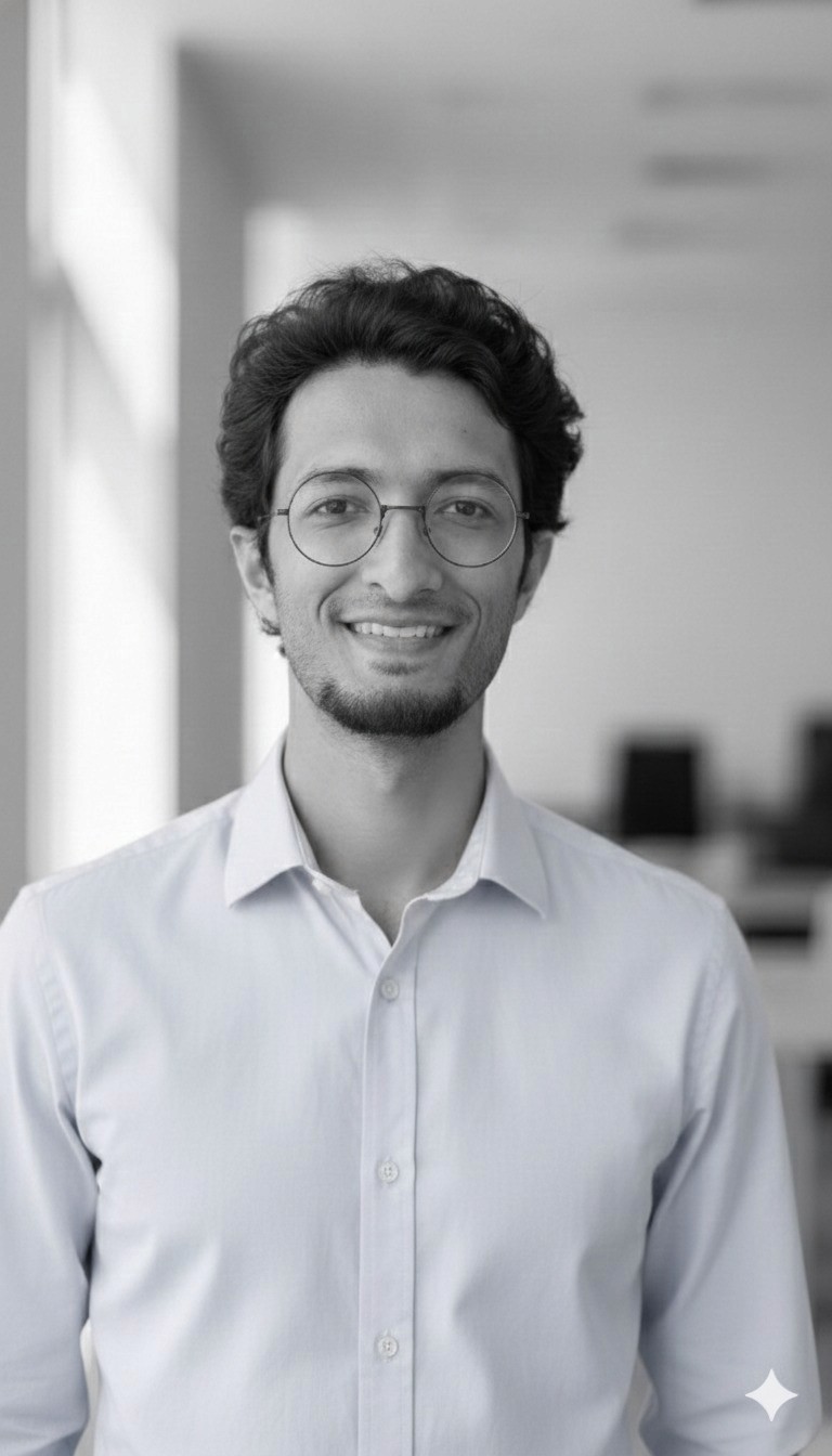 A smiling young man with crossed arms, wearing a plaid shirt and white t-shirt, poses against a dark background.