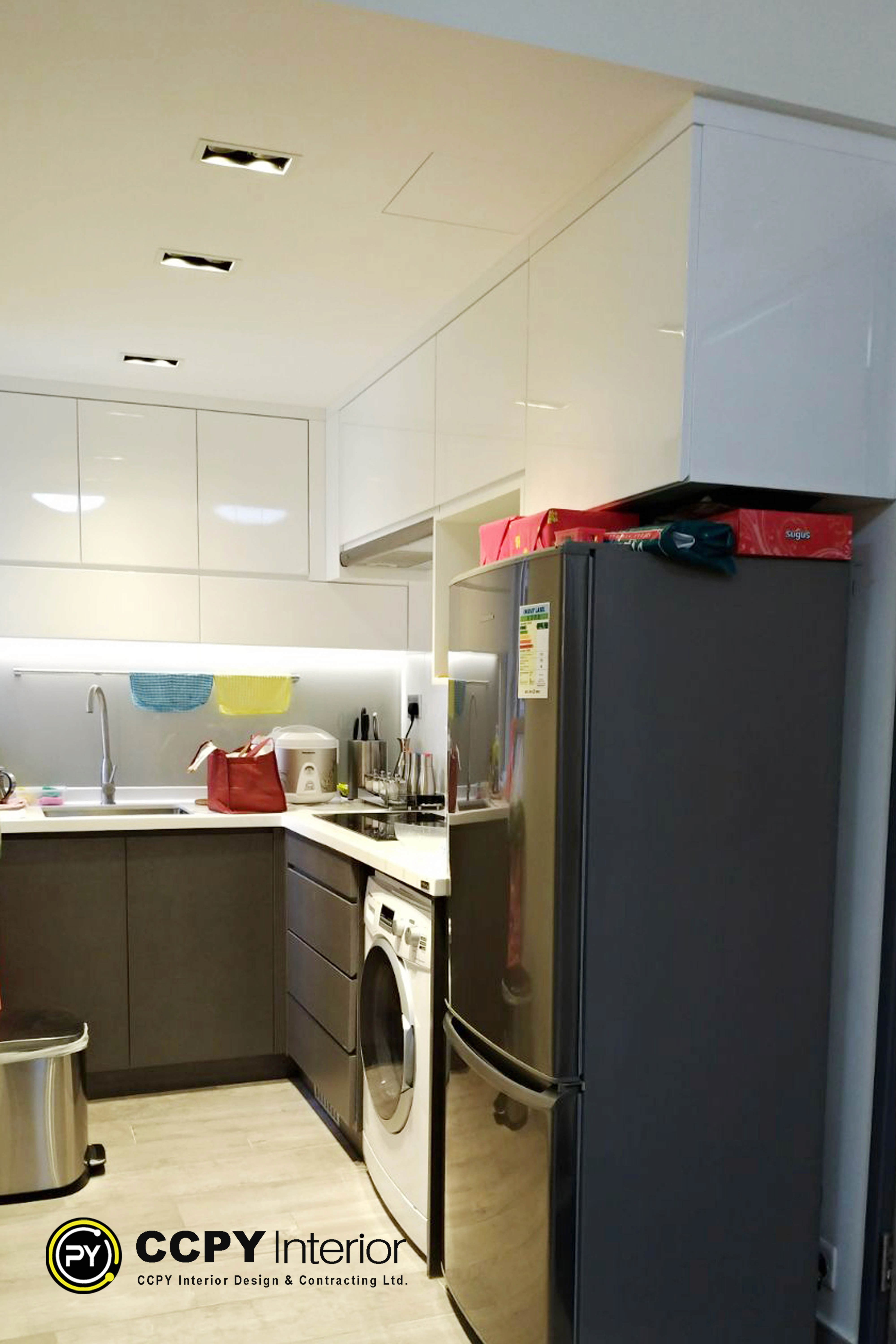 The selected region shows a modern kitchen renovation featuring white upper cabinetry, grey lower cabinetry, a built-in countertop, and integrated appliances.Here are the key design and functional details visible in this layout:Layout & Material SelectionTwo-Tone Cabinetry: Gloss white upper cabinets maximize light reflection, while the lower cabinets feature a contrasting matte grey finish.Under-Cabinet LED Lighting: A continuous LED strip provides functional task lighting across the entire countertop work surface.Compact Integration: A full-sized refrigerator is placed adjacent to the main counter, utilizing top space for additional item placement.Functional ZonesWet Zone: Features an undermount stainless steel sink paired with a high-arc gooseneck faucet.Cooking/Prep Zone: Includes small countertop appliances like a rice cooker, situated right next to a built-in induction or glass-top cooktop.Backsplash: A clean, white minimalist backsplash ties the upper and lower elements together smoothly.