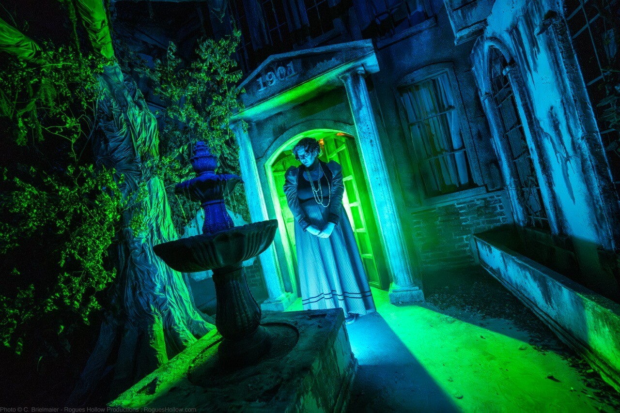 Costumed actor at a green-lit entrance to a decaying orphanage