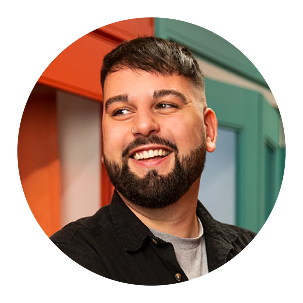 Person wearing a black button-up shirt over a light gray t-shirt, standing indoors in front of colorful red and teal door frames.
