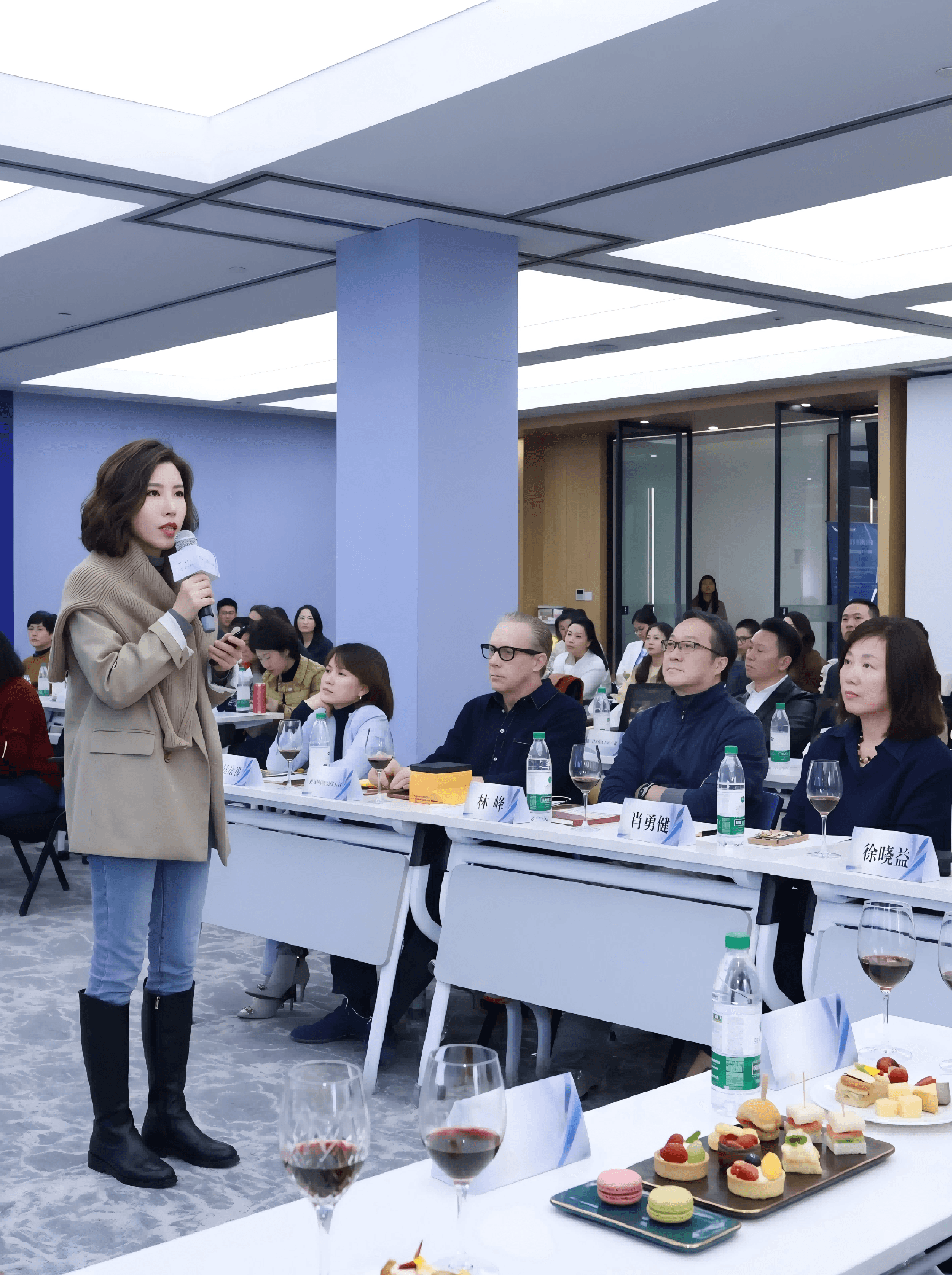 投資者路演活動現場，主講嘉賓在台上發表簡報，台下投資者一邊享用紅酒與輕食一邊專心聆聽，體現高端商務接待與專業發佈 Investor roadshow event with speaker on stage and audience enjoying wine and canapés in a premium business setting