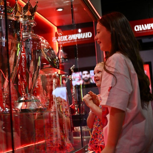 שתי ילדות צעירות מתבוננות בהערכה בגביע כסף גדול המוצג בתוך ויטרינת זכוכית עם תאורה אדומה.