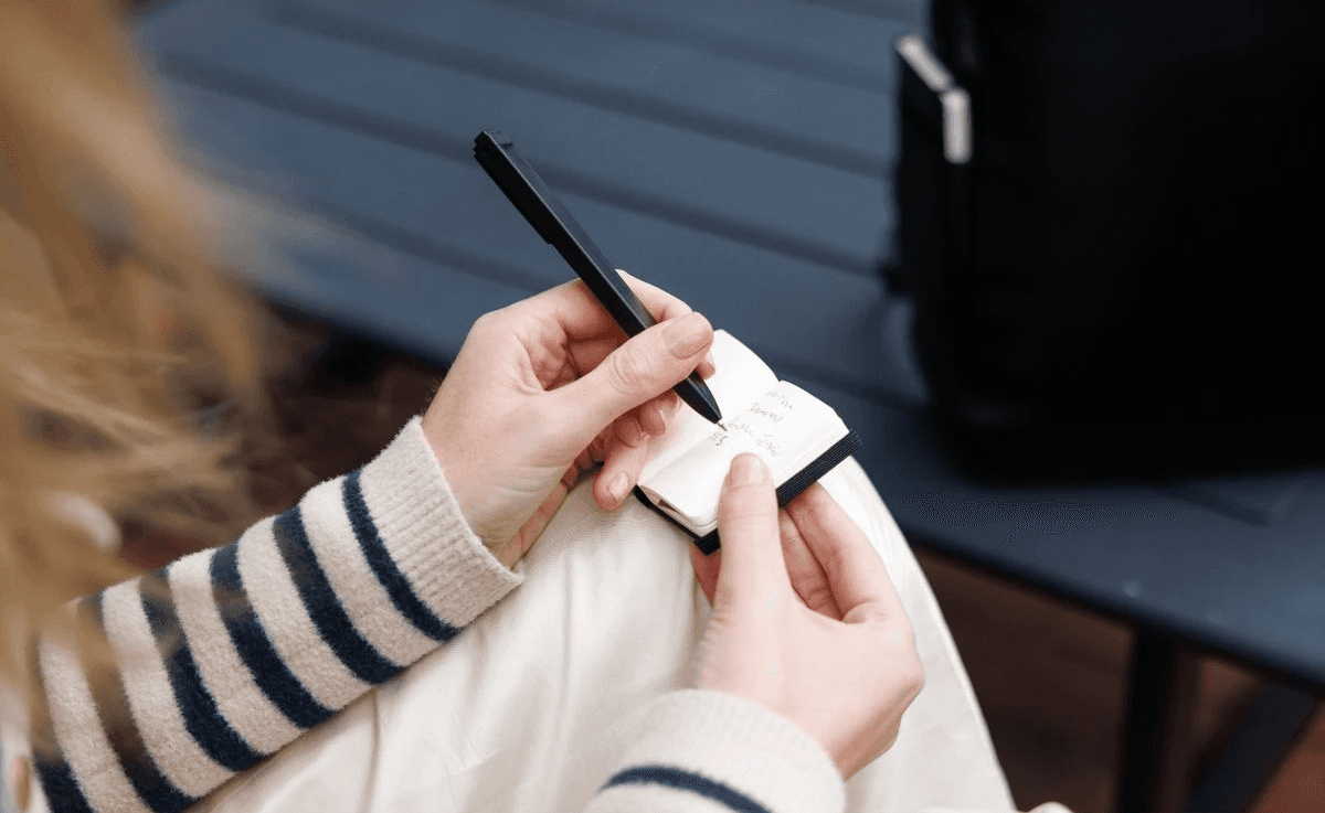 Someone writing in the mini Moleskine notebook keychain with a black ball point pen. 