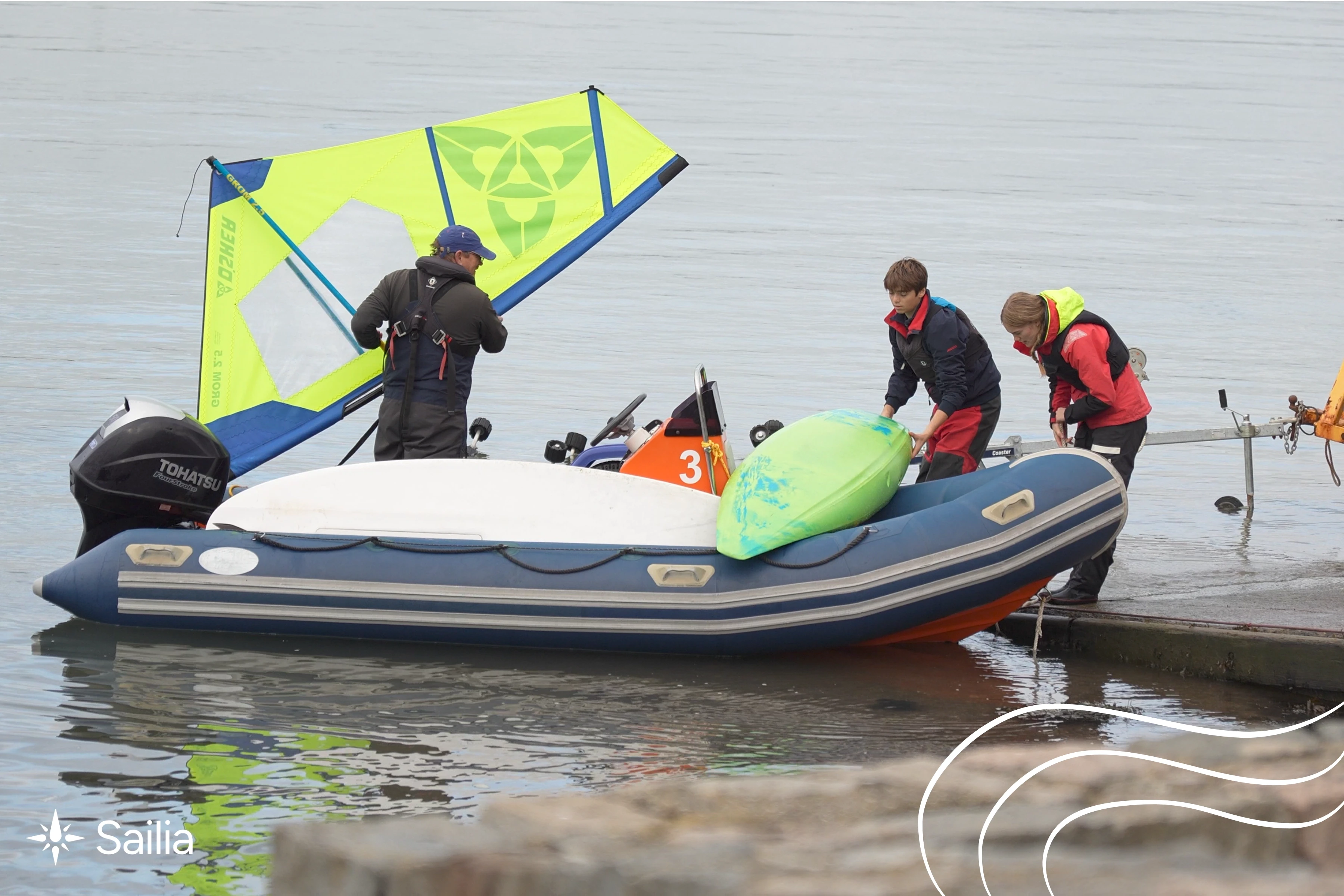 Three people in life jackets stand on a dock beside a dinghy with a yellow sail. One carries a green kayak. The scene is calm and focused.