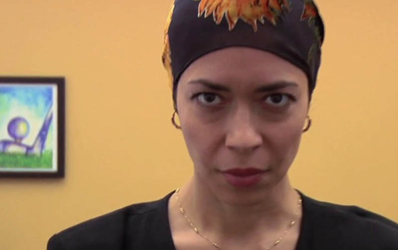 A photo of a woman wearing a hat while in a background a modern painting is hanged on a wall