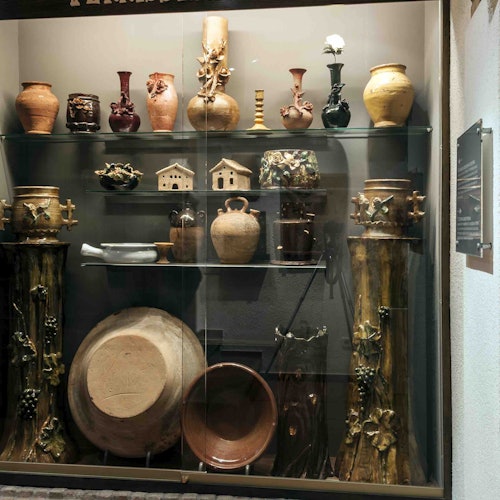 展示柜中陈列着各种陶瓷罐、花瓶和碗,放在玻璃搁板上。底部可见一些大罐子和装饰柱。