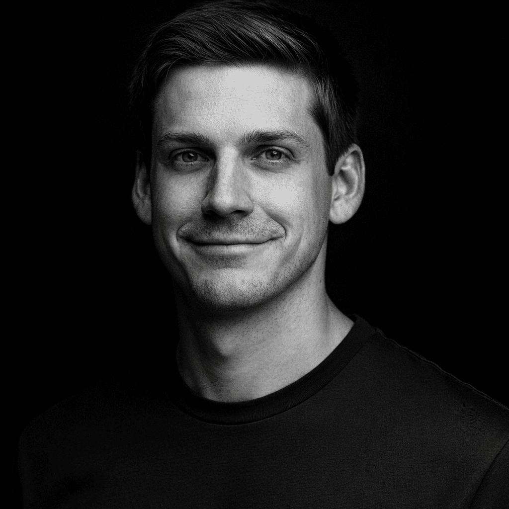 Portrait of a young man with short hair, wearing a dark t-shirt, against a plain background.
