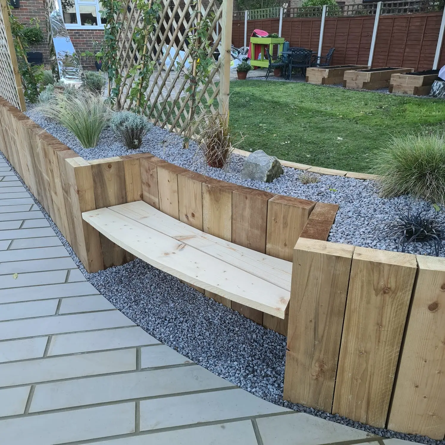 A curved wooden bench surrounded by planters in a landscaped outdoor area.