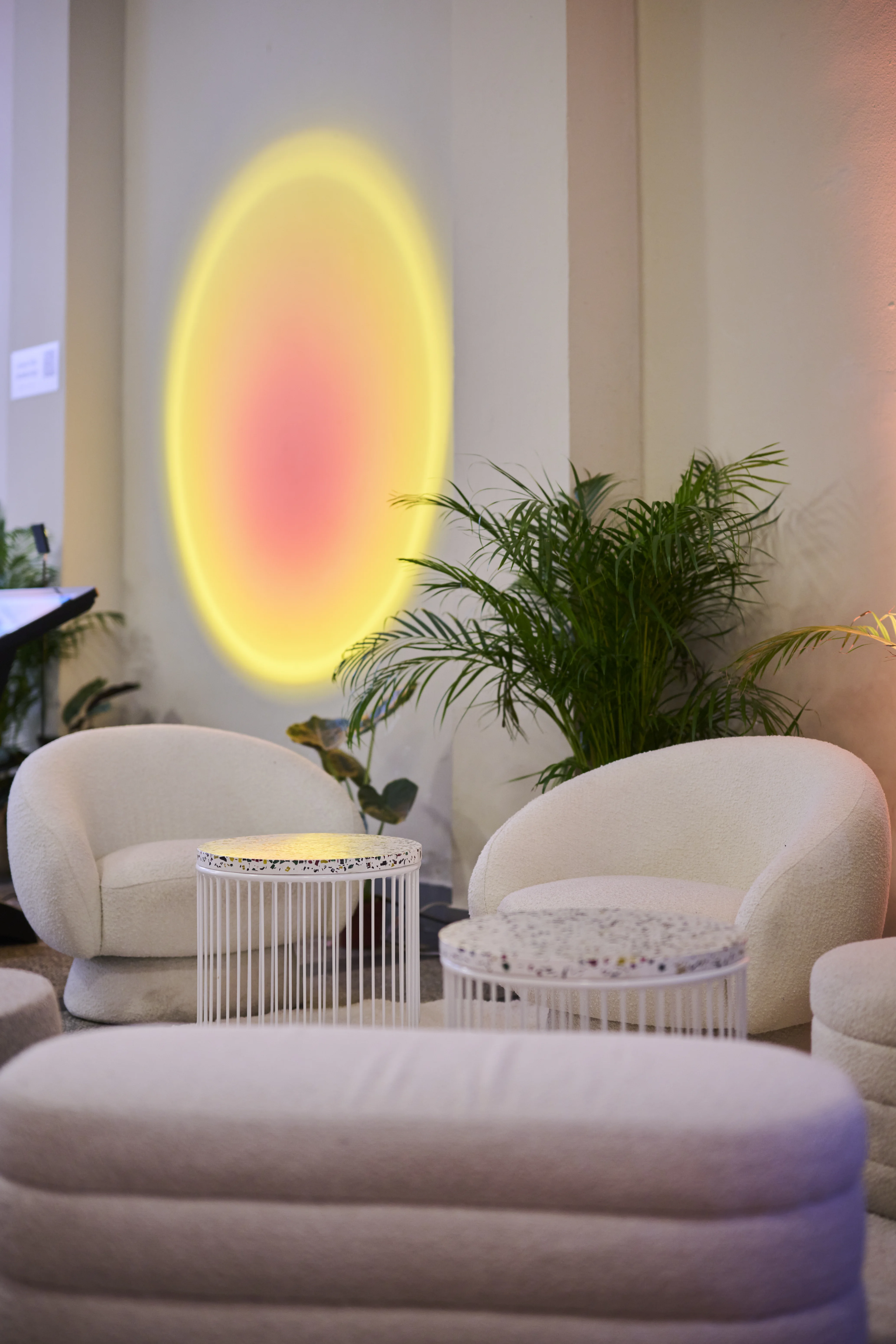 Lounge with cream bouclé armchairs, terrazzo side tables, palm and sunset light circle.