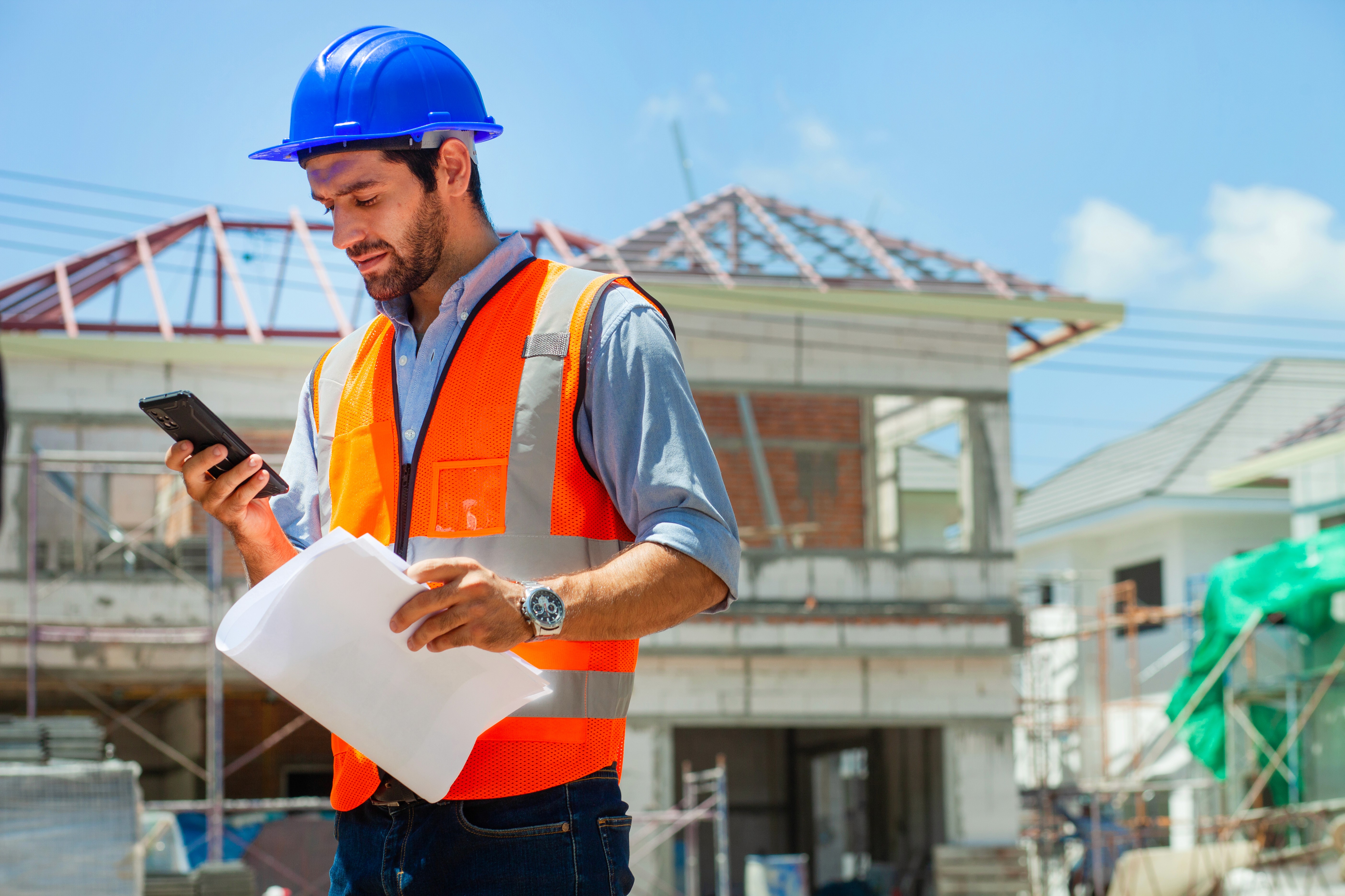 Contractor using smartphone on modern construction site to manage project
