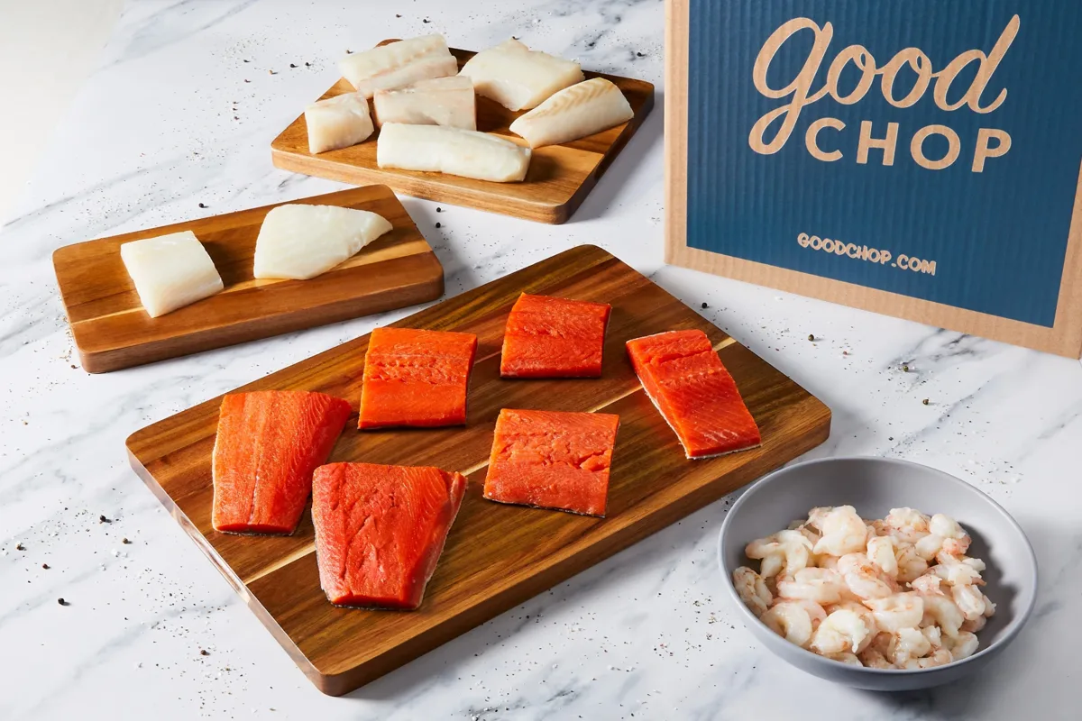 Salmon, white fish, and shrimp on cutting boards next to a Good Chop box