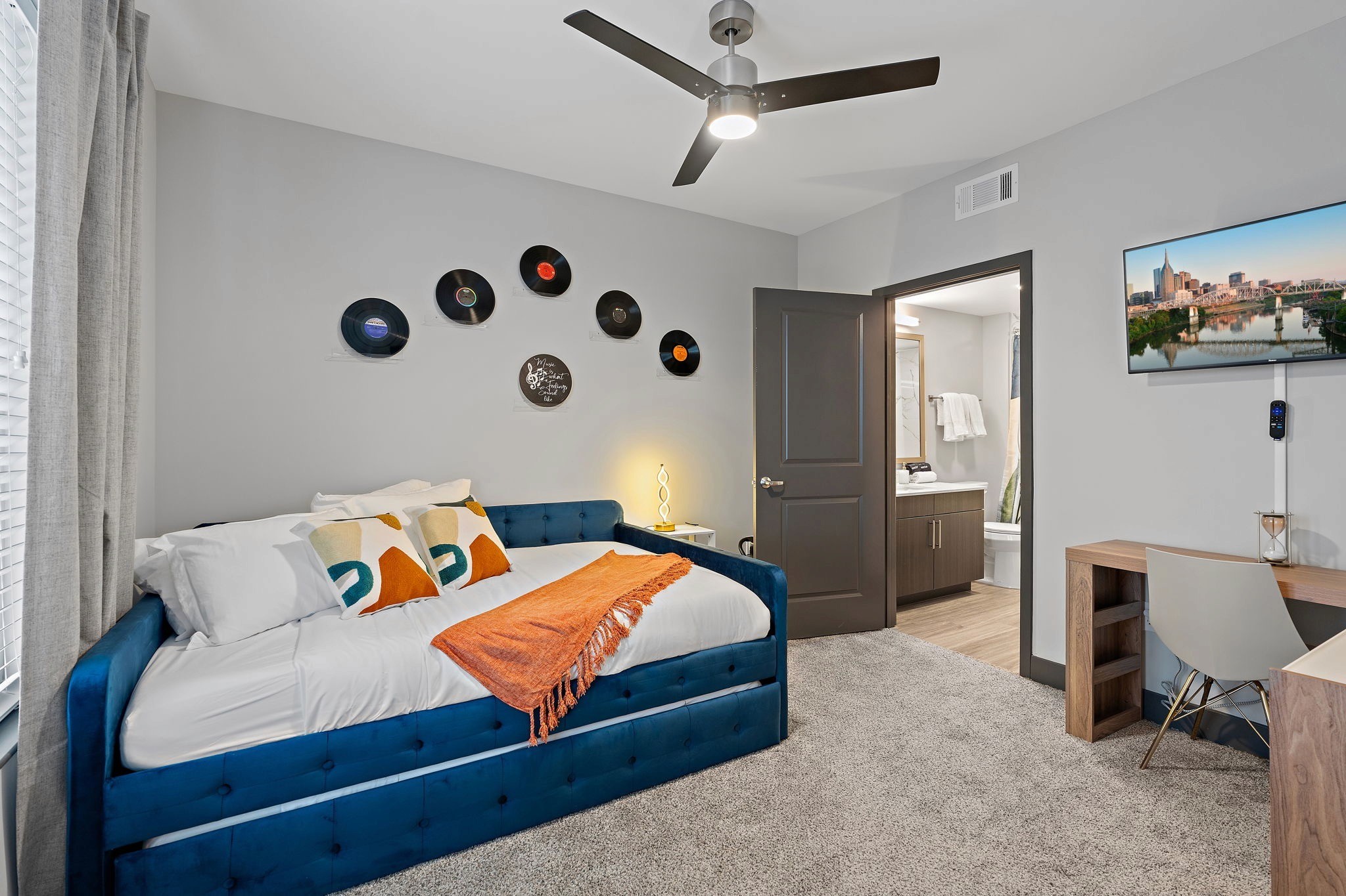 Modern bedroom with blue upholstered bed, vinyl record wall decor, workspace, and ensuite bathroom.