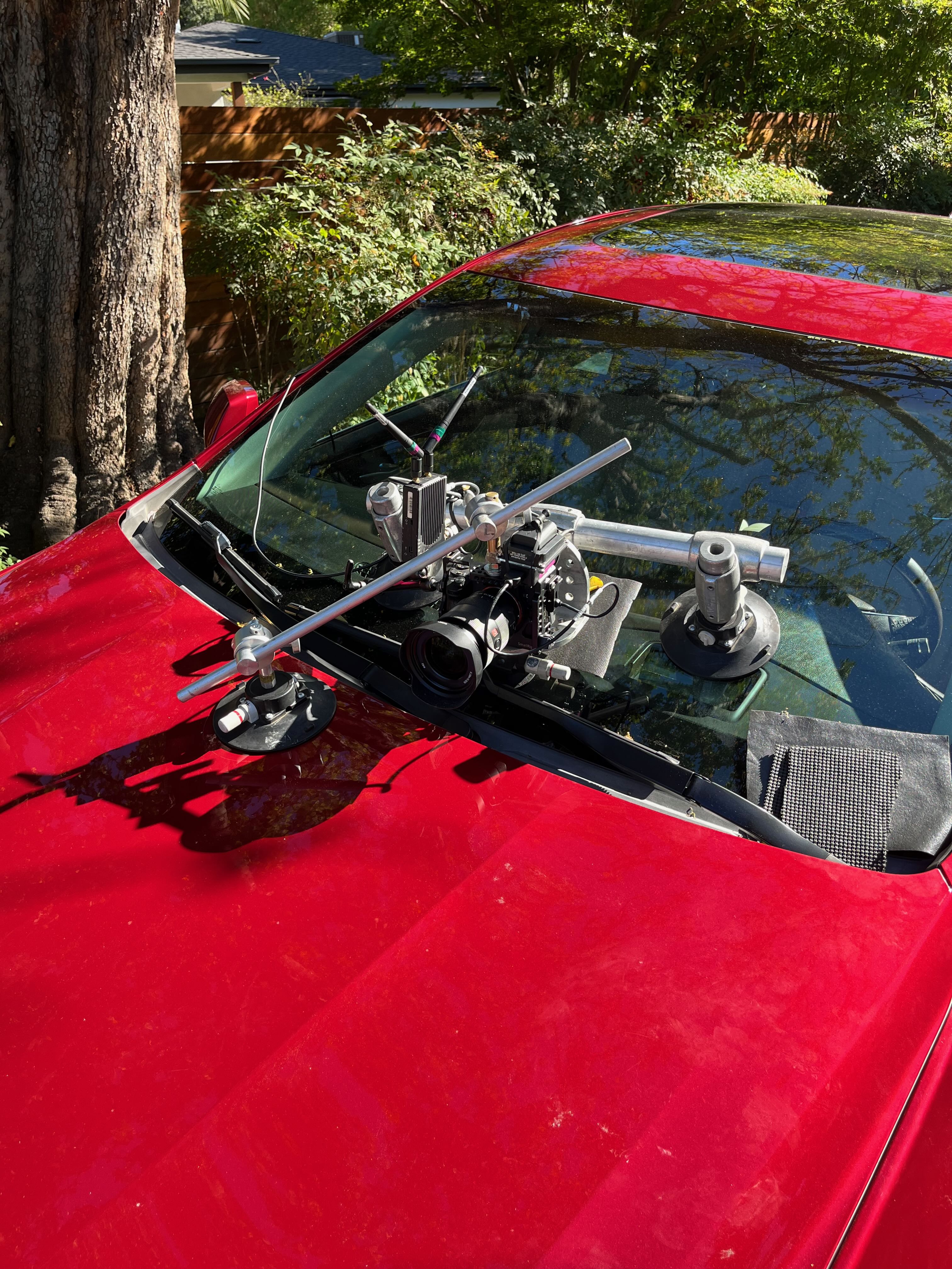 Close-up of a cinema camera secured to a red car’s hood and windshield with suction cups and support rails