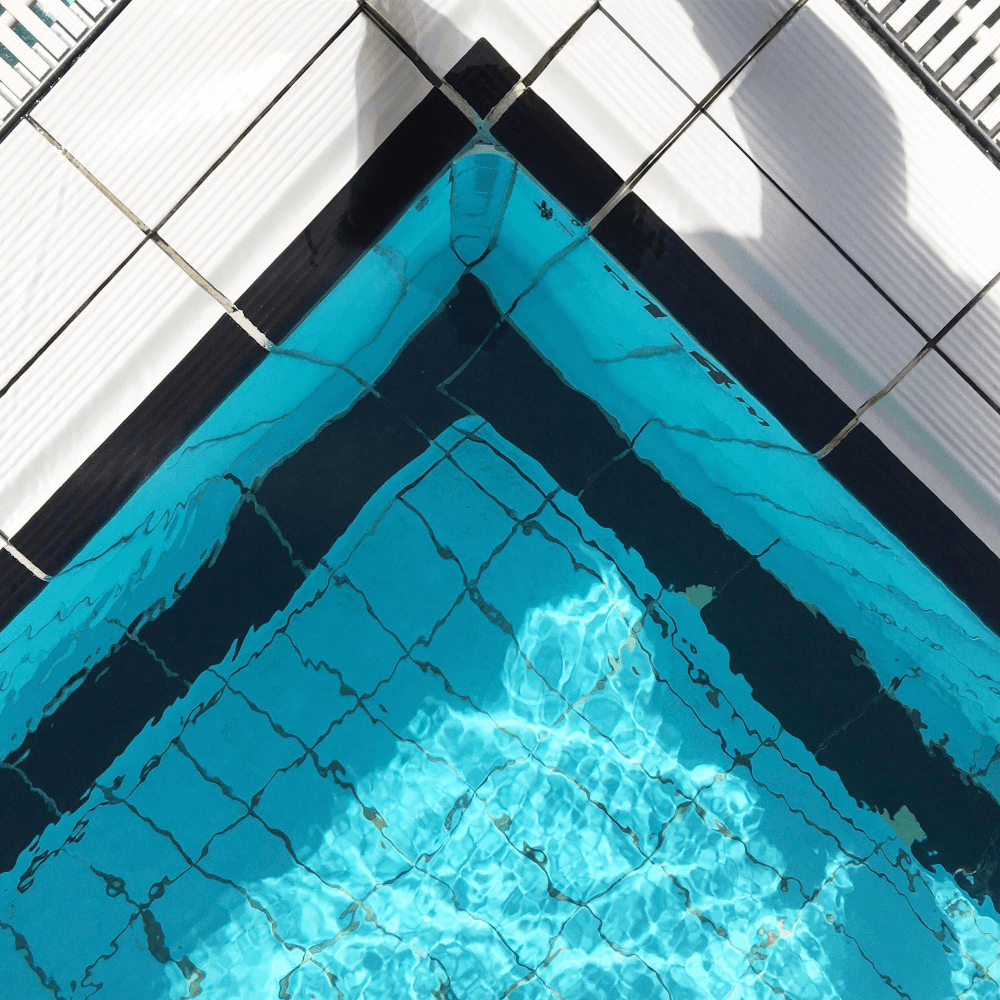 Top-down view of a geometric swimming pool with clear blue water and sharp tile patterns.