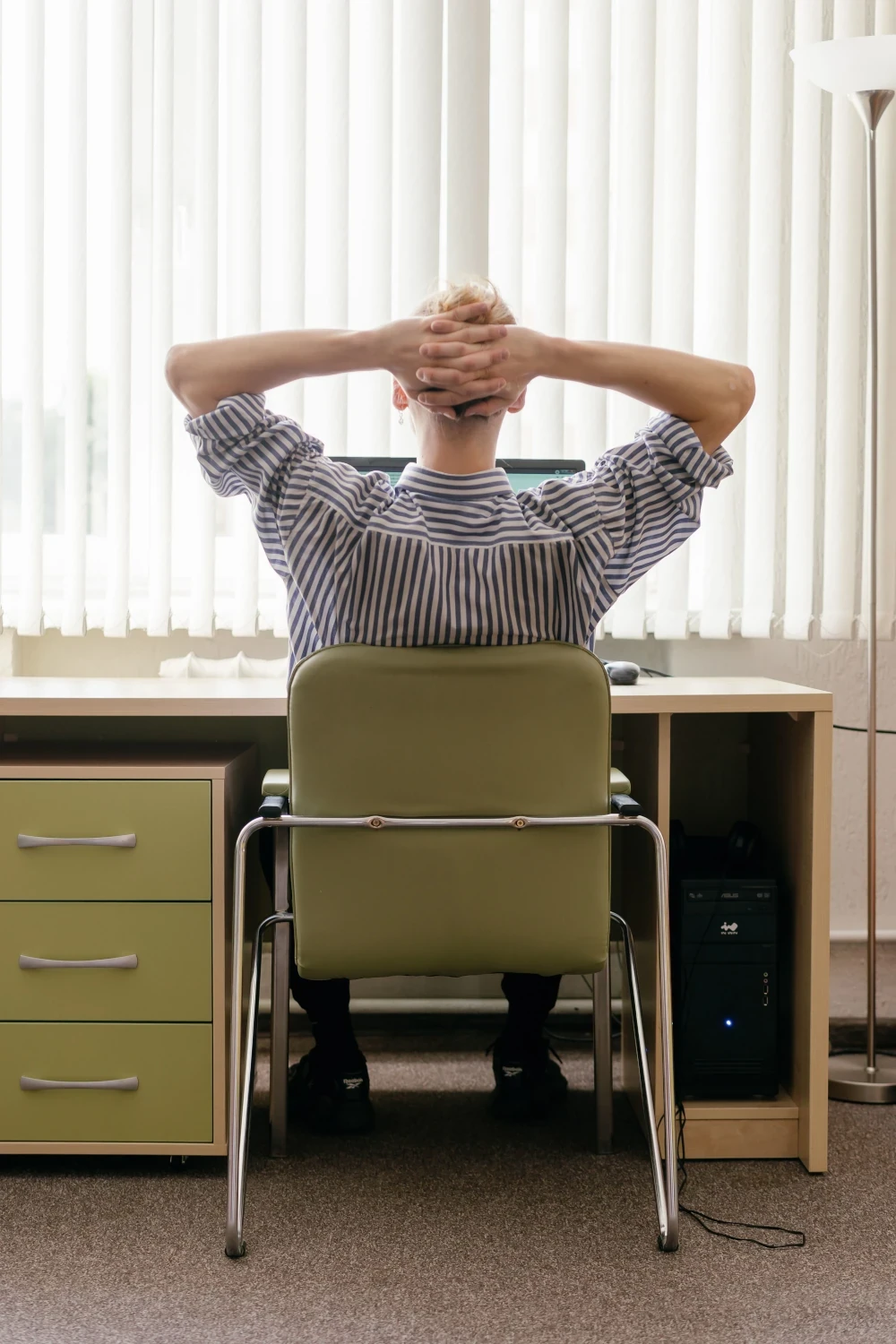 Person seated at a desk with their hands behind their head, appearing tense and overwhelmed.