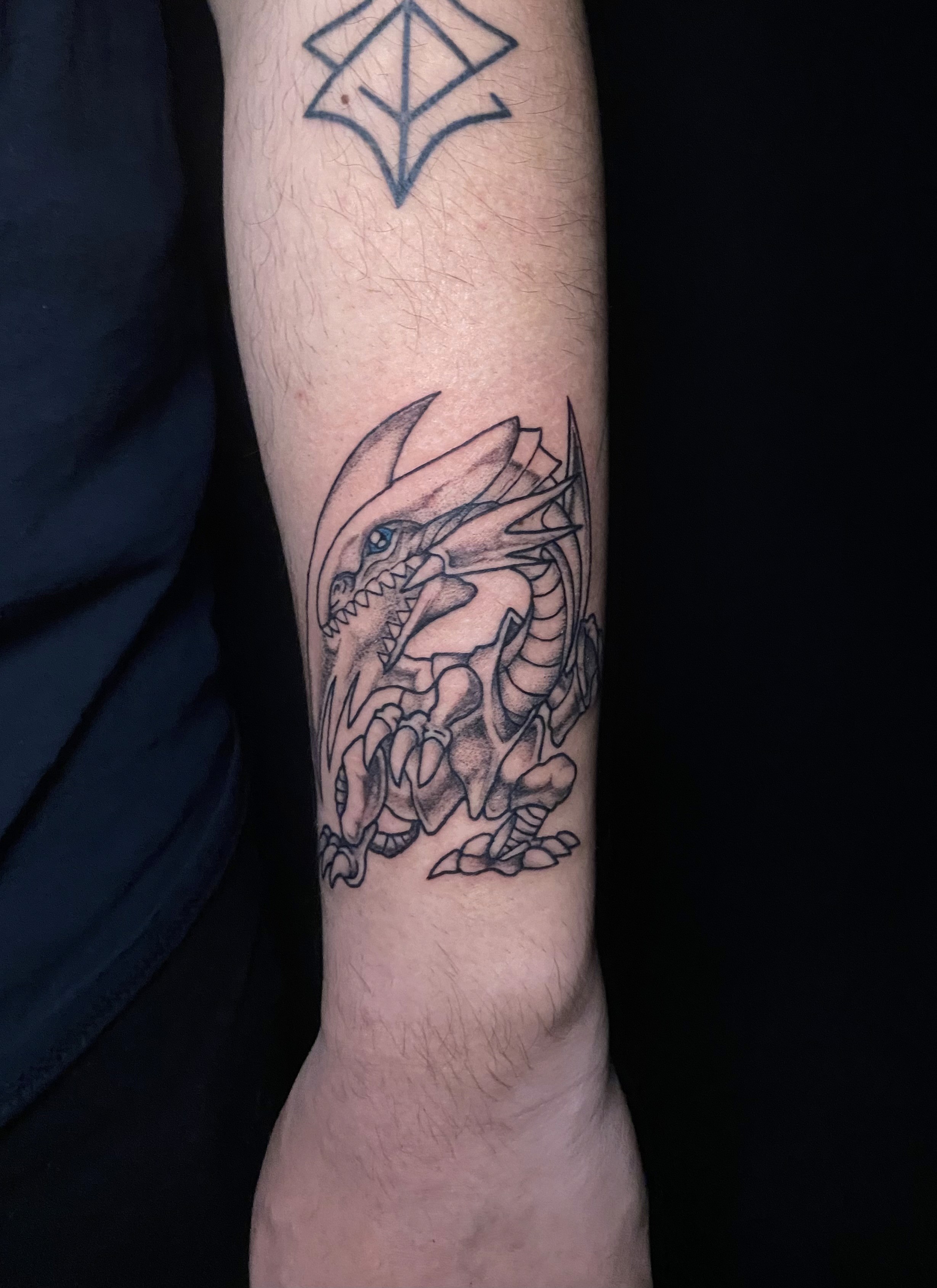 A vibrant tattoo of a chainsaw-like creature on a person's forearm. The tattoo is detailed with shades of orange, black, teal, and red.