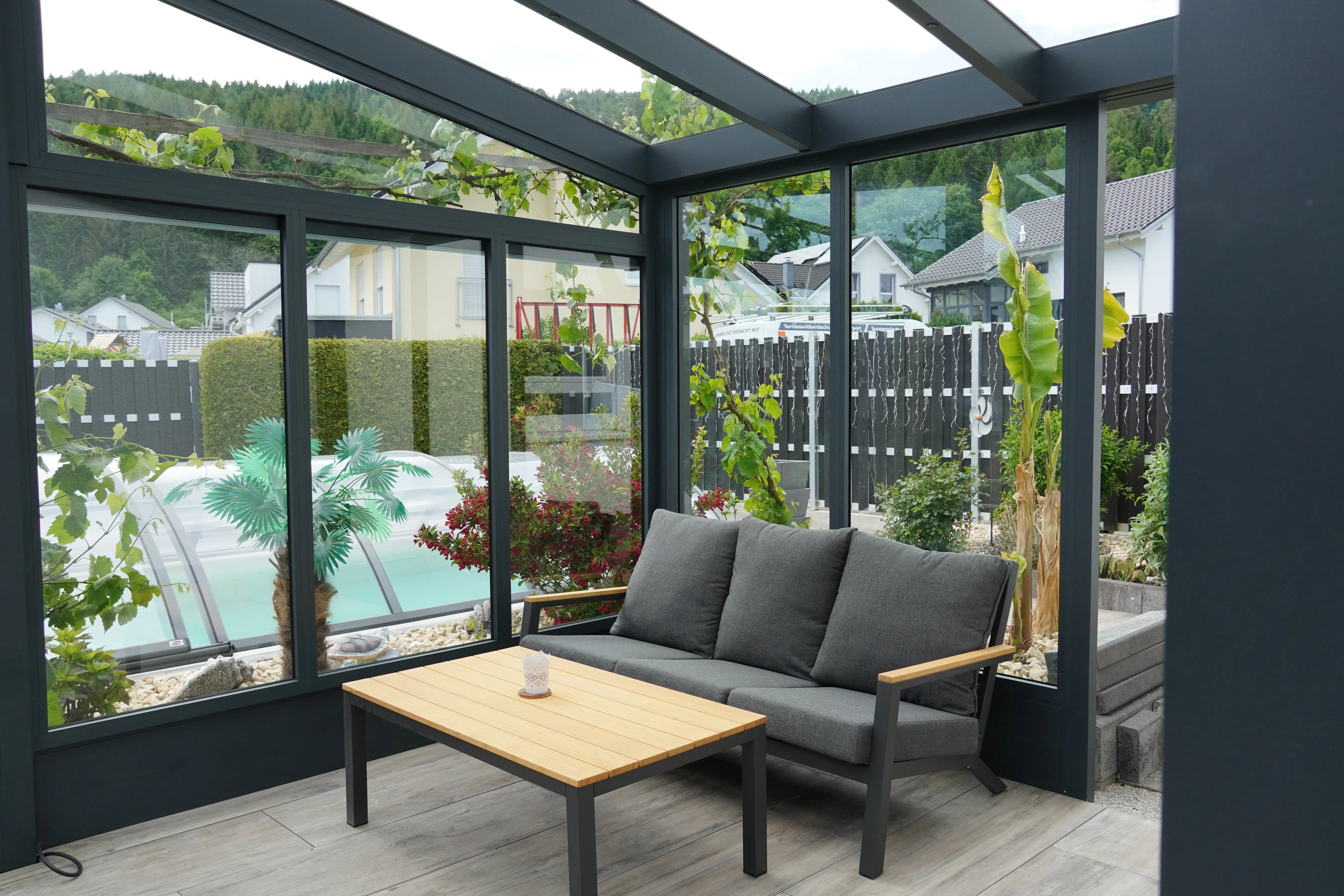 Kaltwintergarten aus Glas mit Loungesofa und Poolblick im Garten