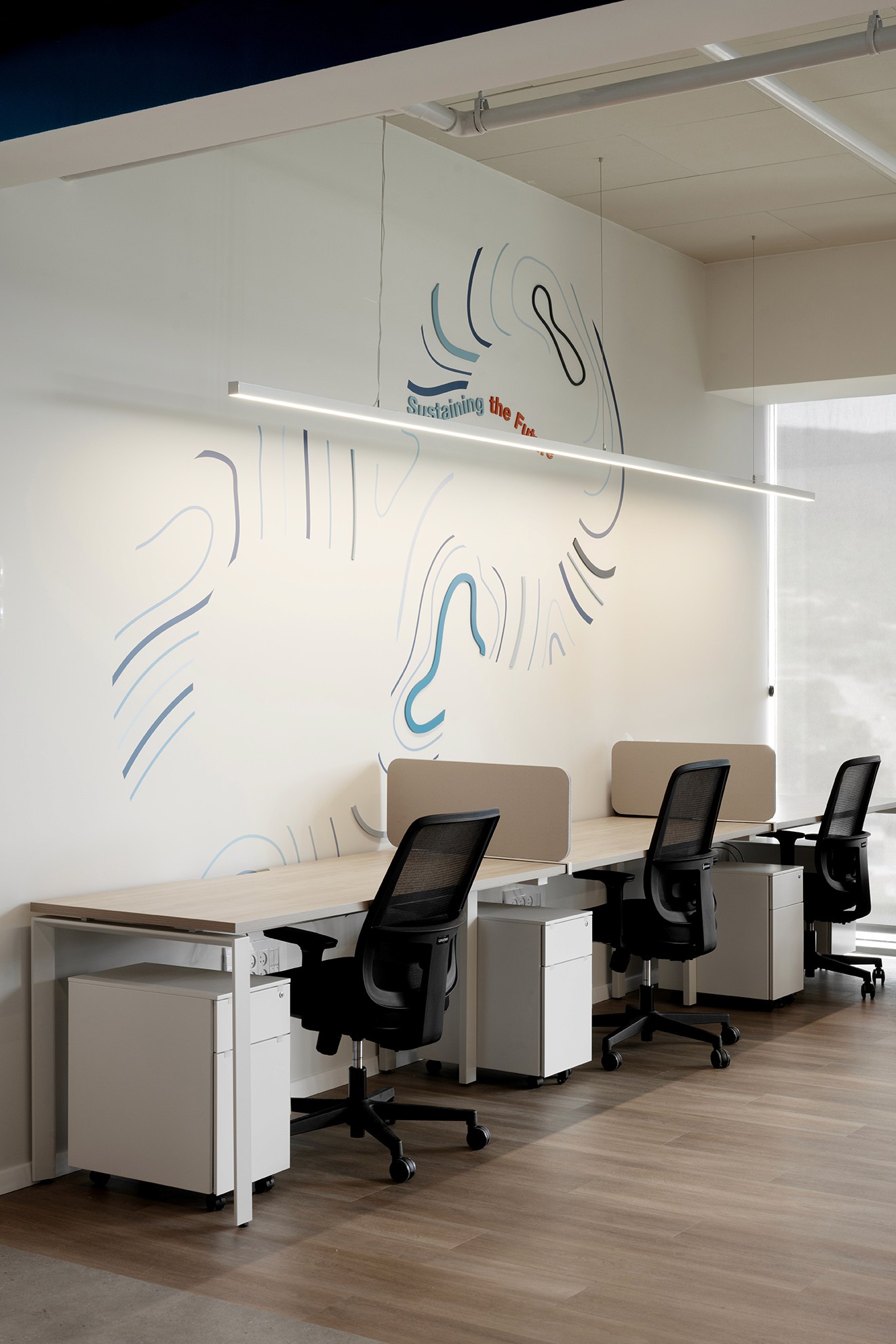 משרד צוותי אינטימי: עמדות עבודה ארגונומיות מול קיר ממותג בגרפיקה לינארית – חיבור לשפה העיצובית של החלל הציבורי גם בחדרים הסגורים