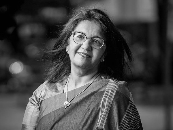 A smiling young woman in a pink blouse stands in an office setting, with soft lighting and a professional backdrop.