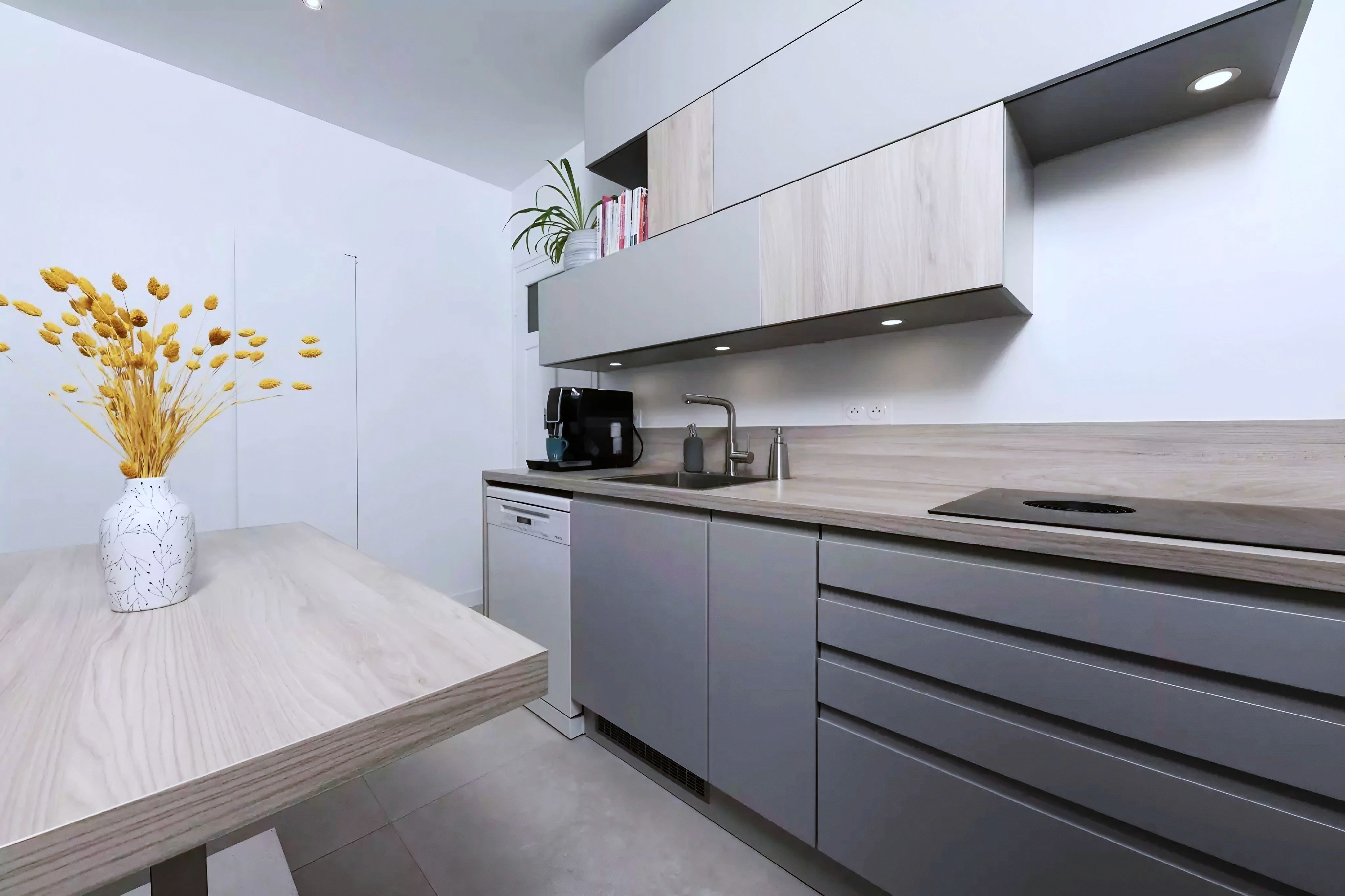 Transformation cuisine 77 avec armoires bois clair et gris, évier encastré, plan travail foncé et éclairage sous armoire, rénovation complète.