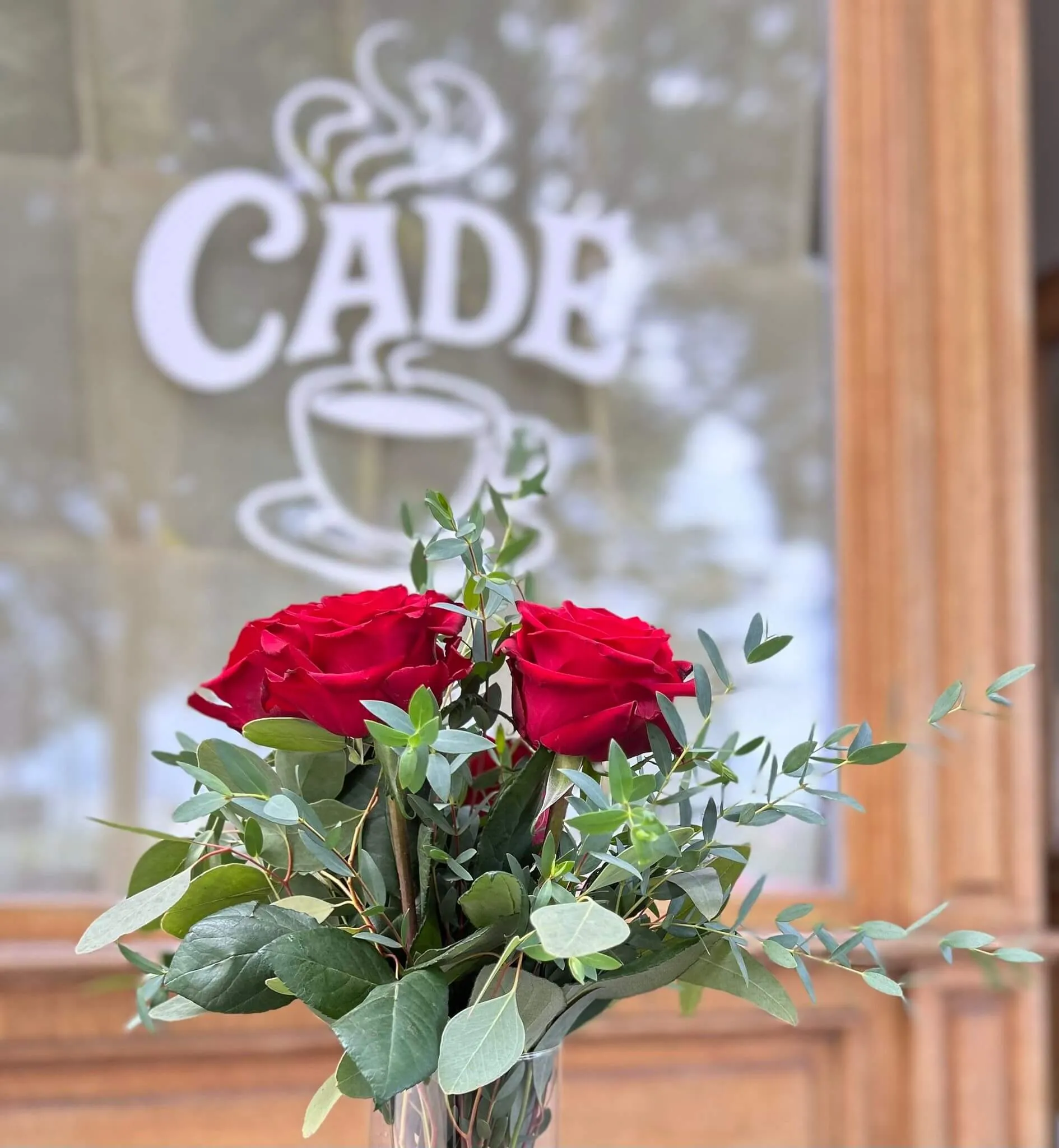 A bouquet of red roses placed in front of a cafe window with the word "CADRA" visible.