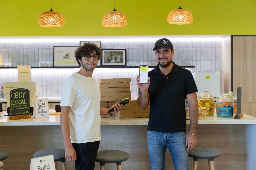 two business owners stand smiling, and they hold Teya card machines