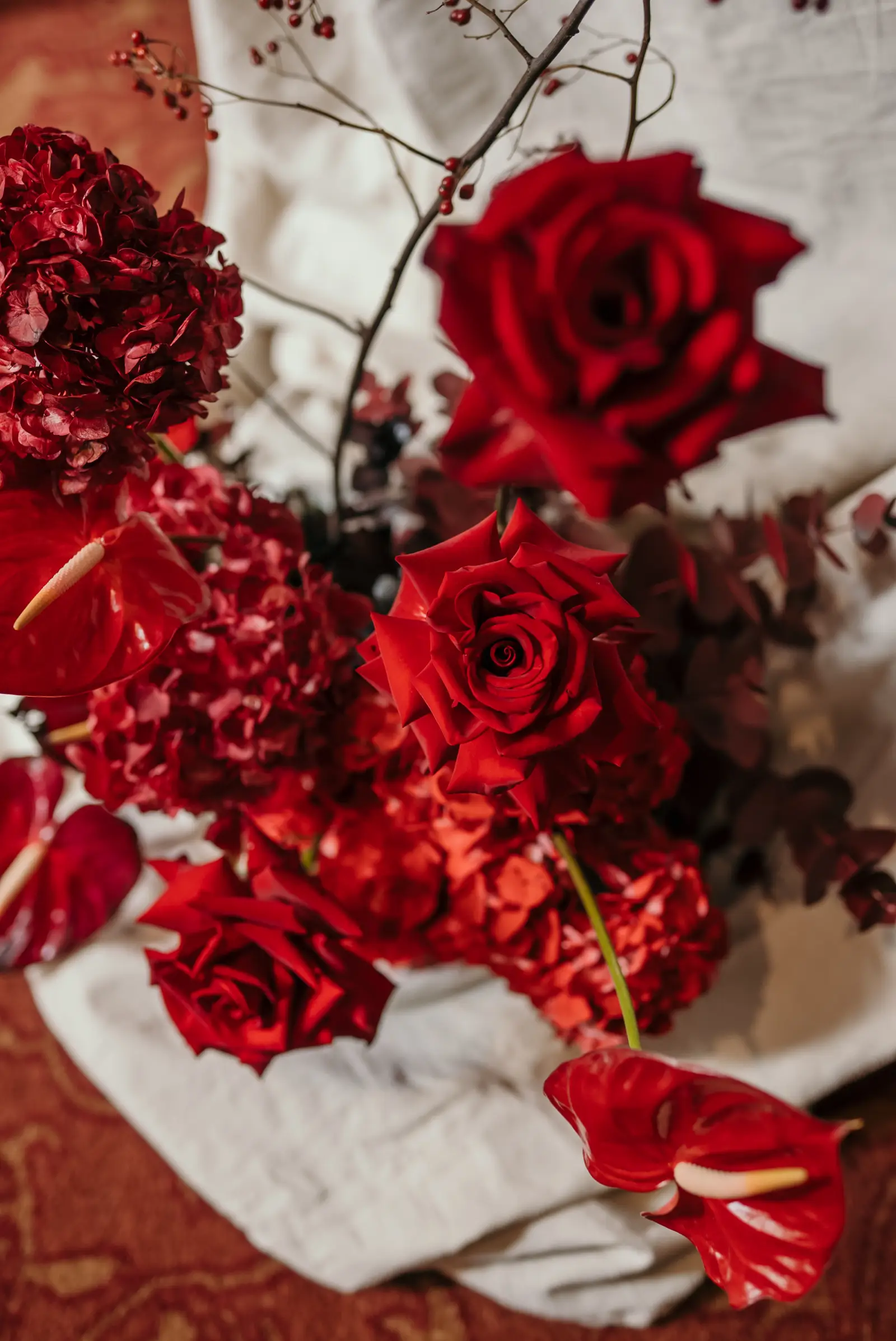 Vista cenital de ramo con rosas rojas, anturios y hortensias sobre mantel de lino blanco en decoración de eventos.