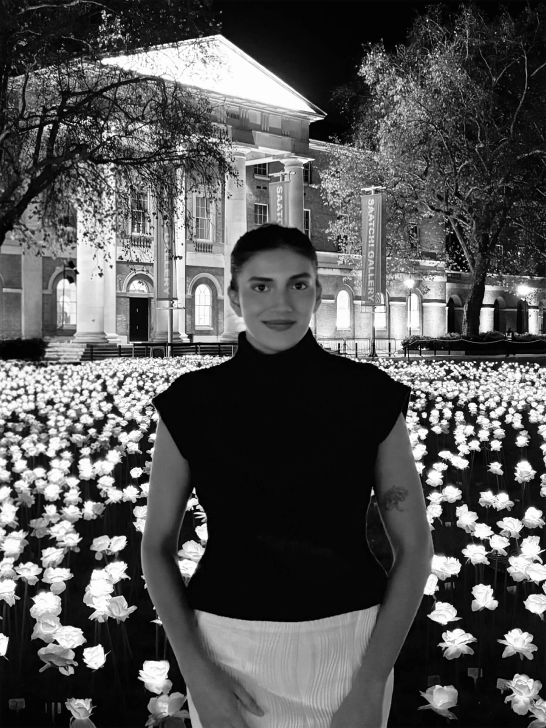 Black-and-white photo of a woman standing in a field of illuminated flowers in front of a gallery building at night.