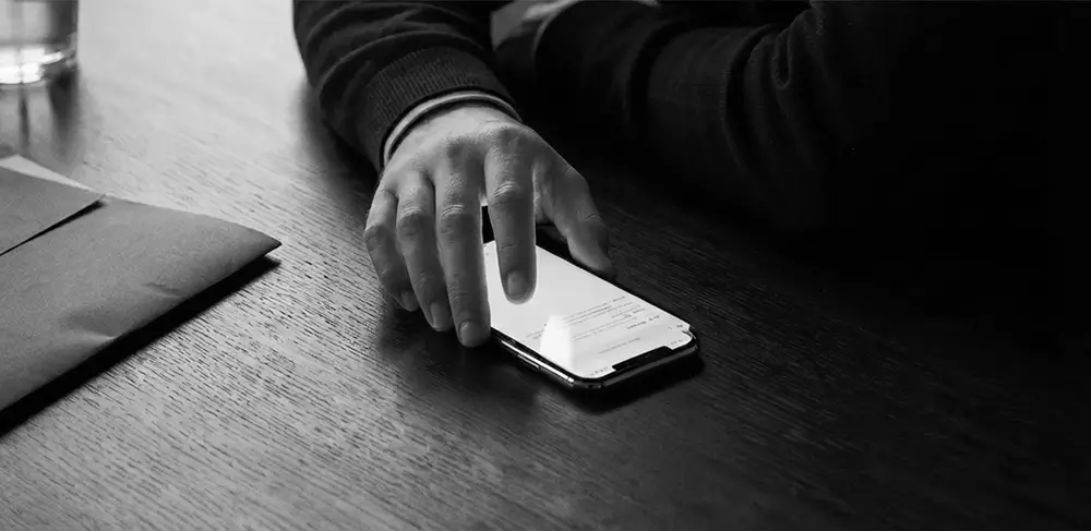 Main saisissant un téléphone sur un bureau en bois, ambiance sombre et contrastée.