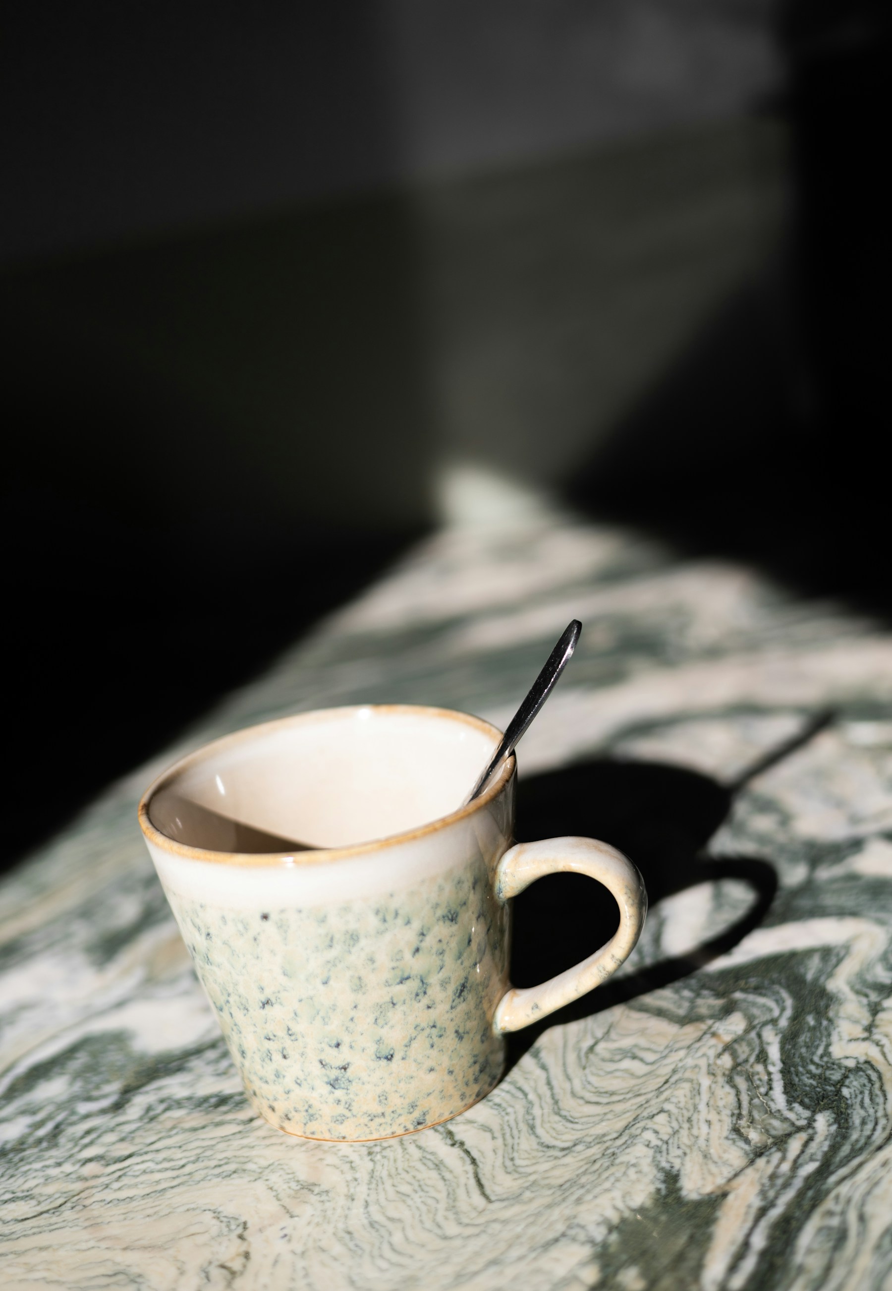 Speckled mug with a spoon casting a long shadow
