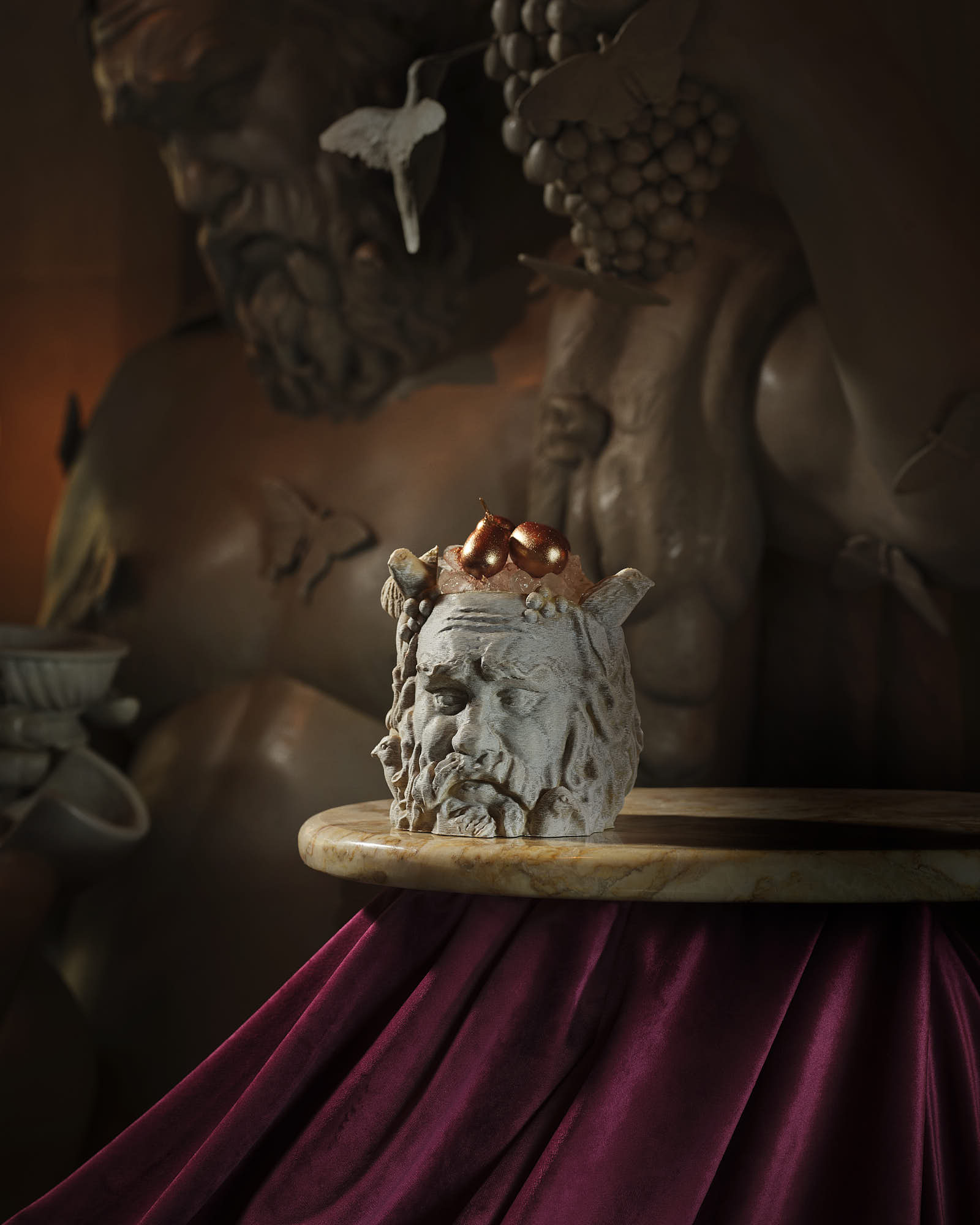 A small, ornate bacchus head rests on a decorative pedestal against a dark backdrop with subtle textures.