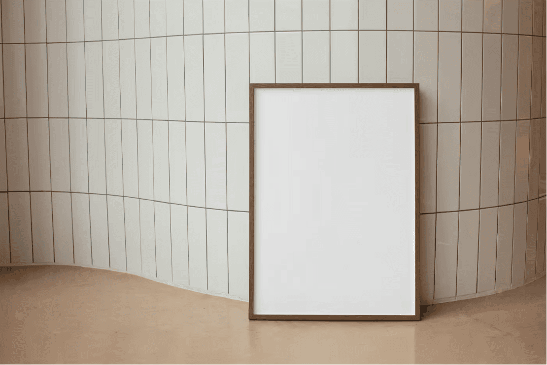 Mockup of a framed poster leaning against a tiled wall with a curved design. The warm, neutral tones and minimalist setting provide a modern, stylish presentation for showcasing artwork or branding.