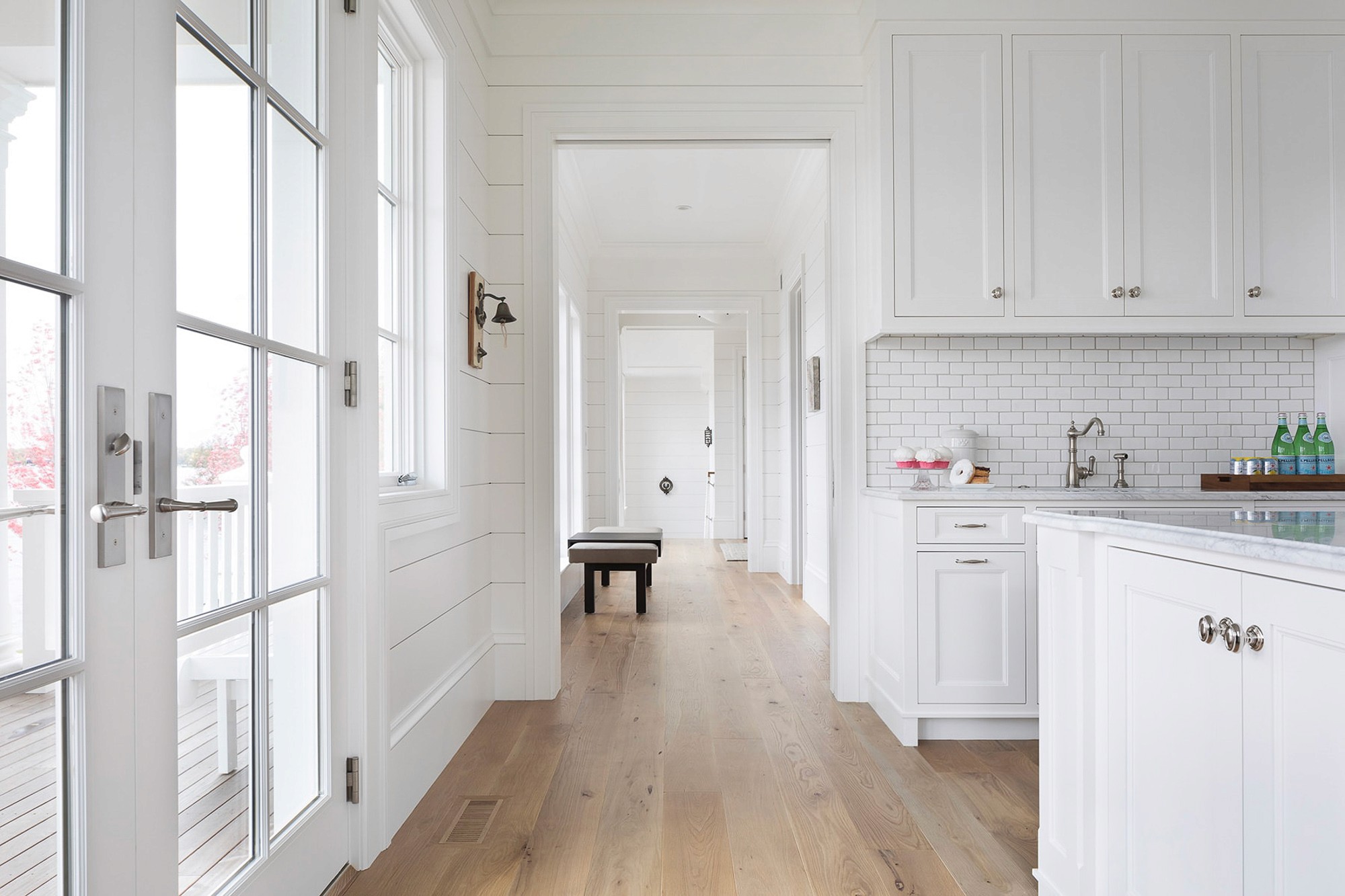 A bright, all-white colonial-style home interior with a kitchen area and hallway.