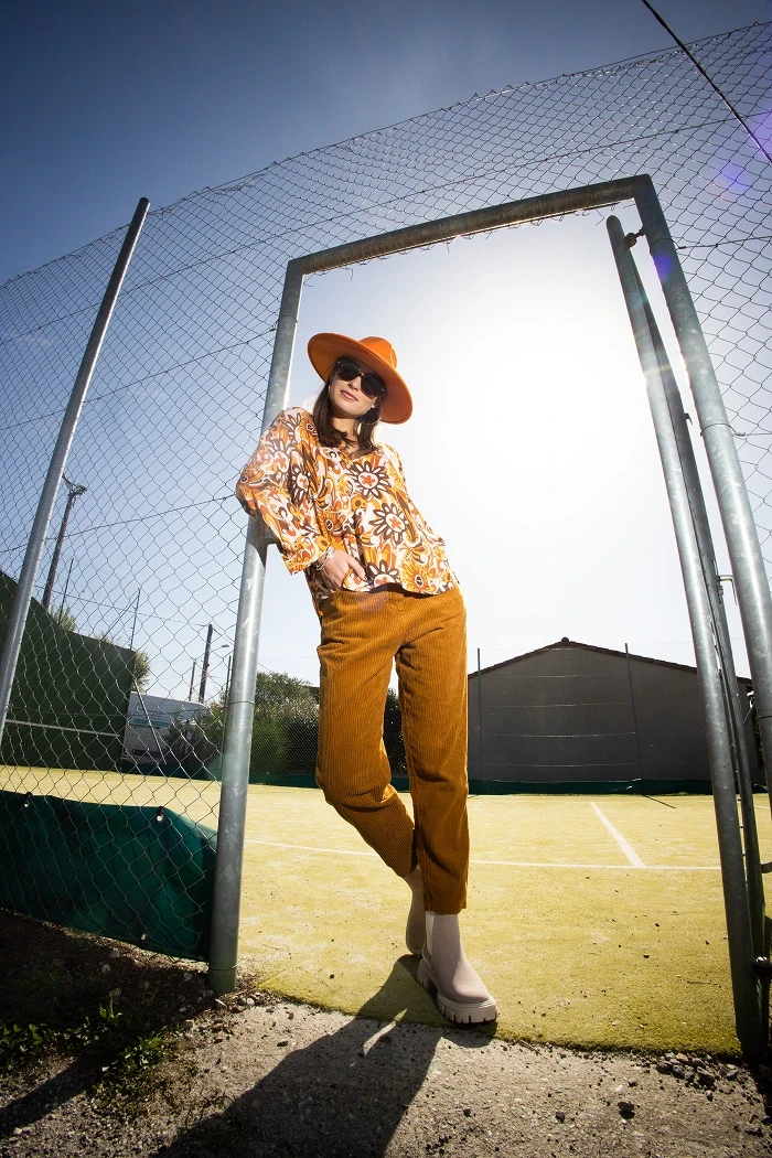 Une femme en tenue orange rétro pose à l’entrée d’un court de tennis
