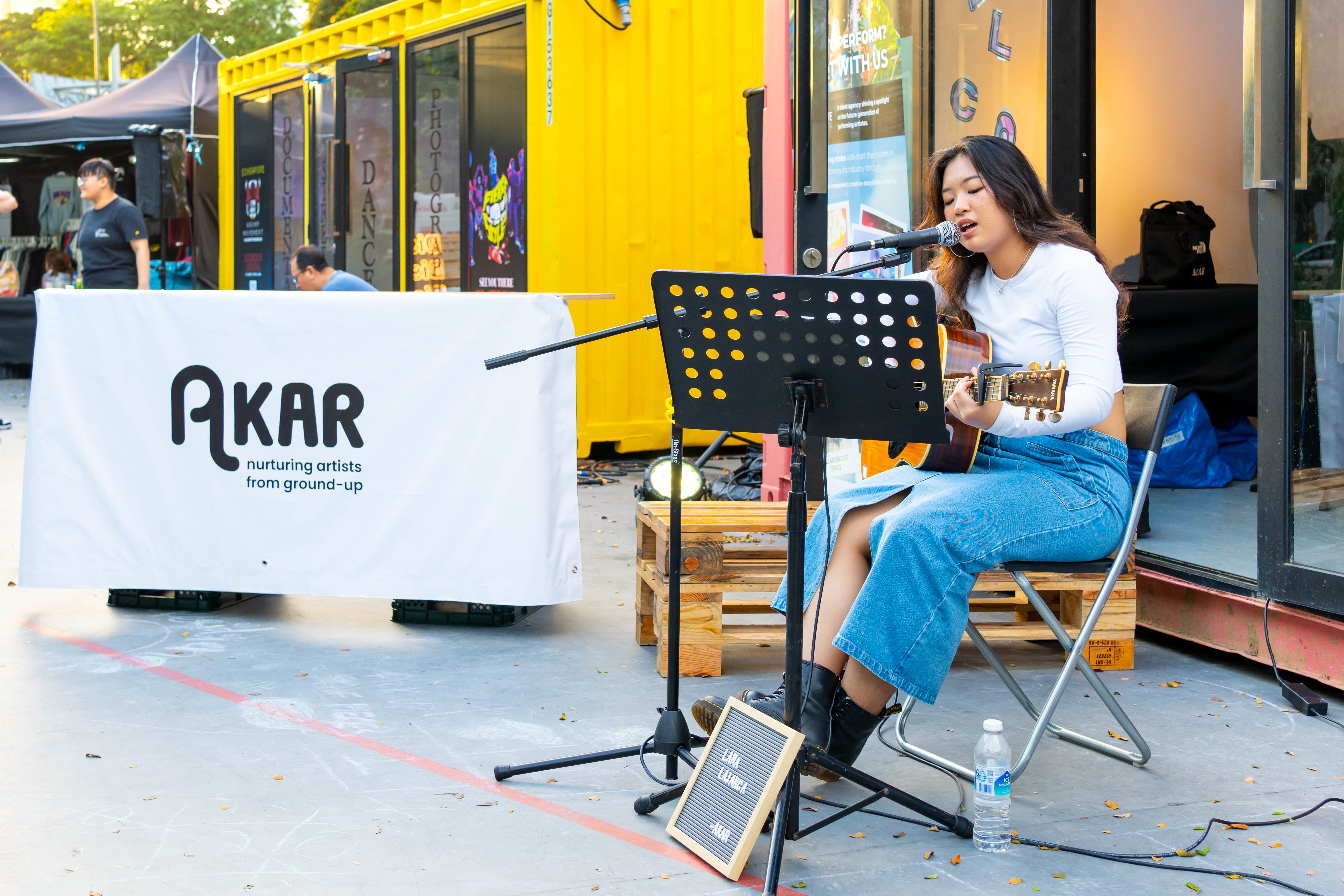 Lana Lajarca singing at *SCAPE COMMA Creative Arts Festival with a guitar.