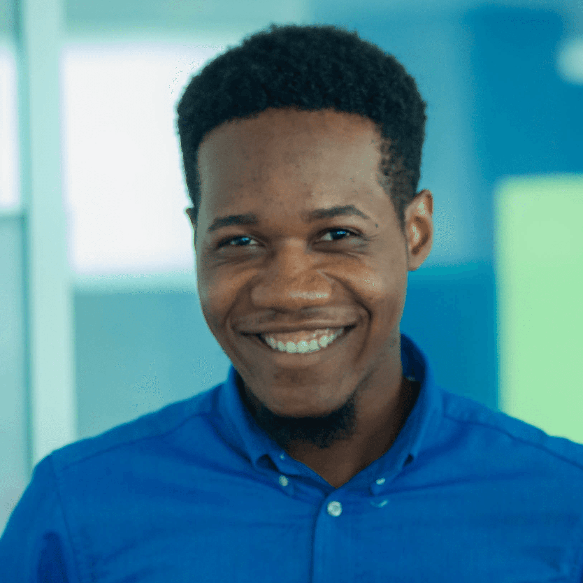 Smiling young man in a blue shirt with a teal background.