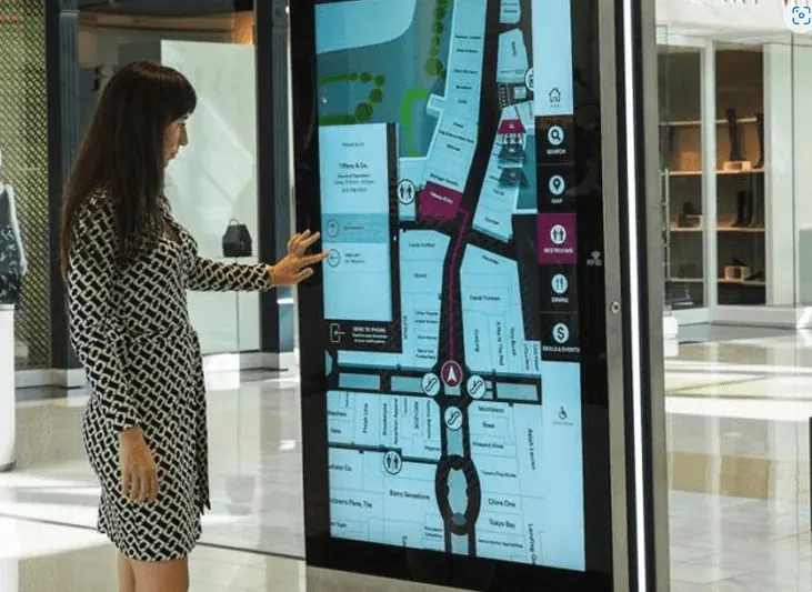 Awoman using a wayfinder kiosk at a simon mall