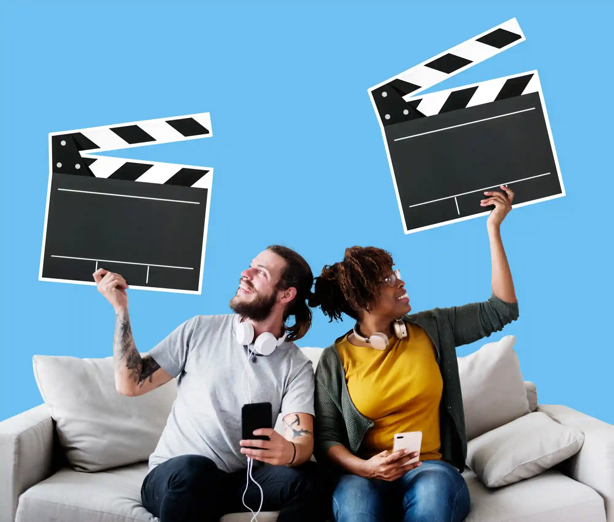 Two people sitting on a couch holding up movie clapperboards, illustrating a fun home-streaming or film-making experience.