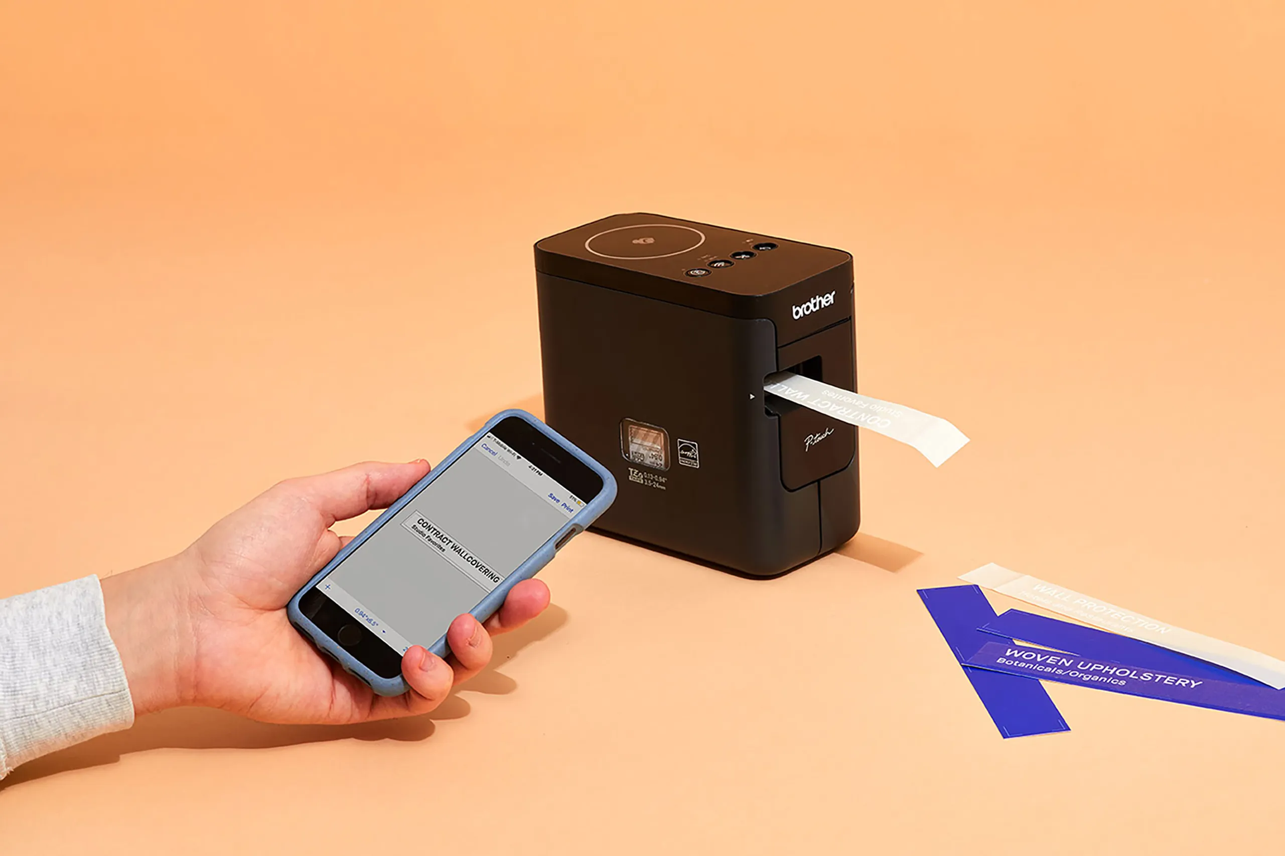 Hand using a smartphone beside Wolf-Gordon material sample labeling equipment