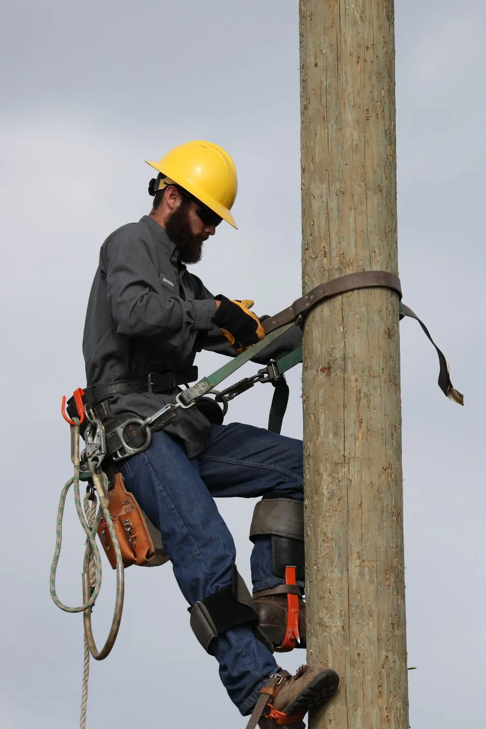 An electrician skillfully climbs a tall wooden power pole.